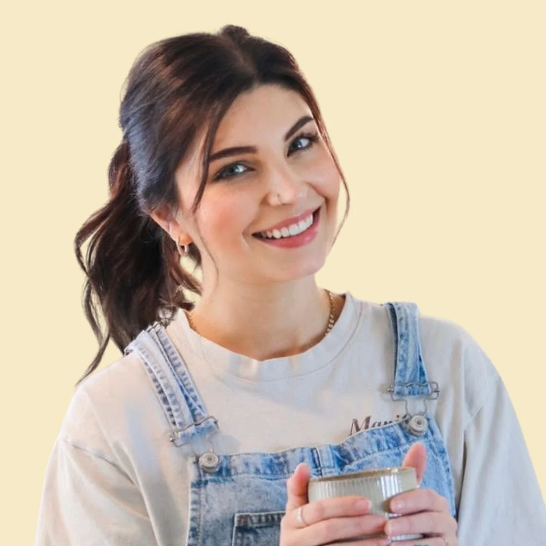 A smiling woman with brown hair, wearing a white top with overalls, against a butter yellow background.
