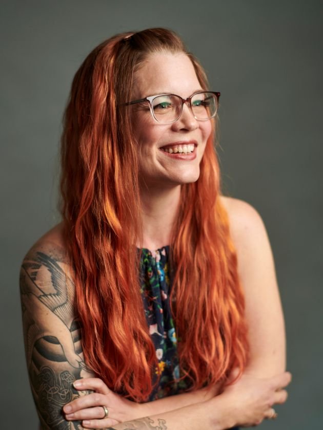 Sara is a 40-something woman with long, wavy red hair in this photo. She's wearing glasses, ad smiling in slight profile.