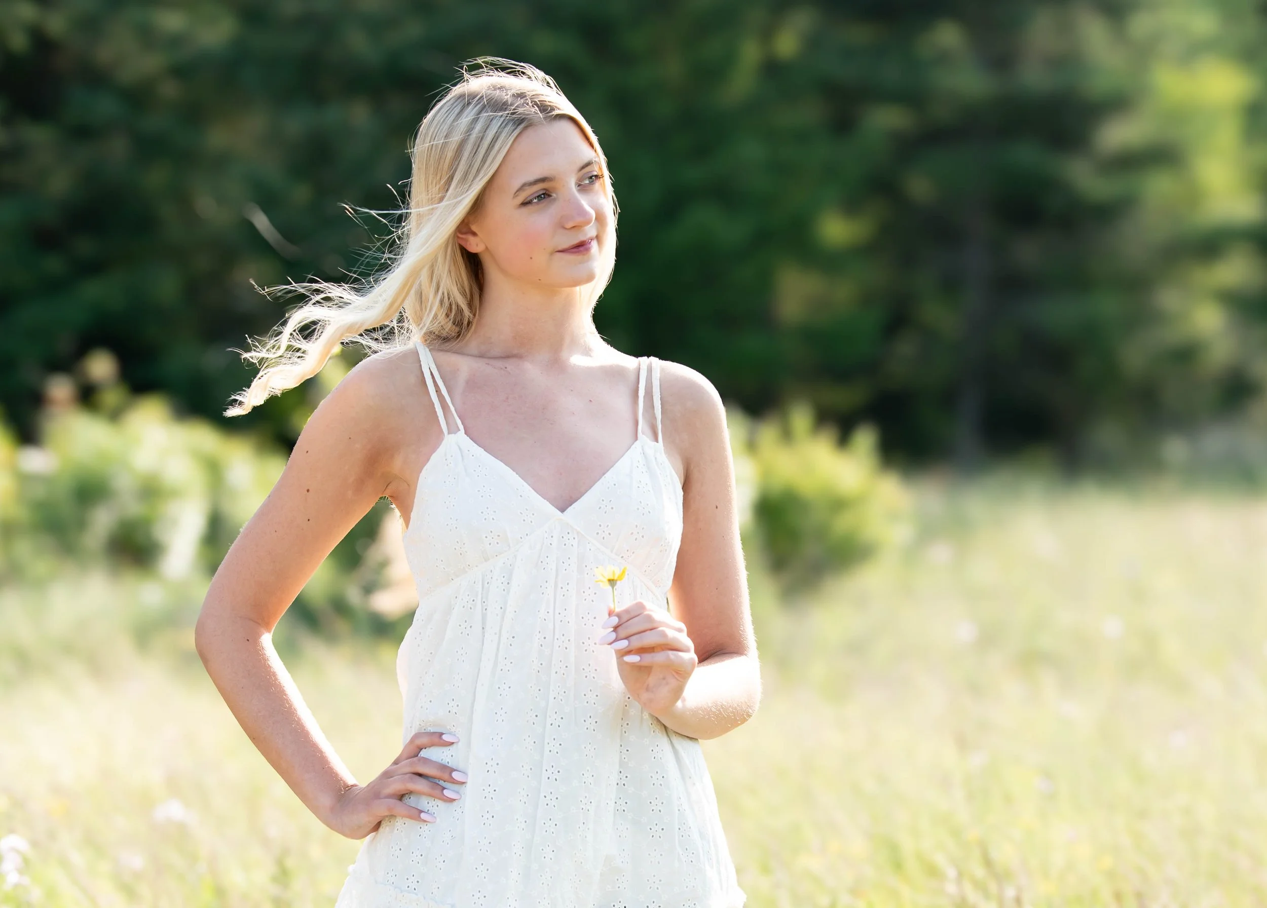 Senior High School Photoshoot, standing in a grassy field holding a small flower with trees in the background. Portland OR
