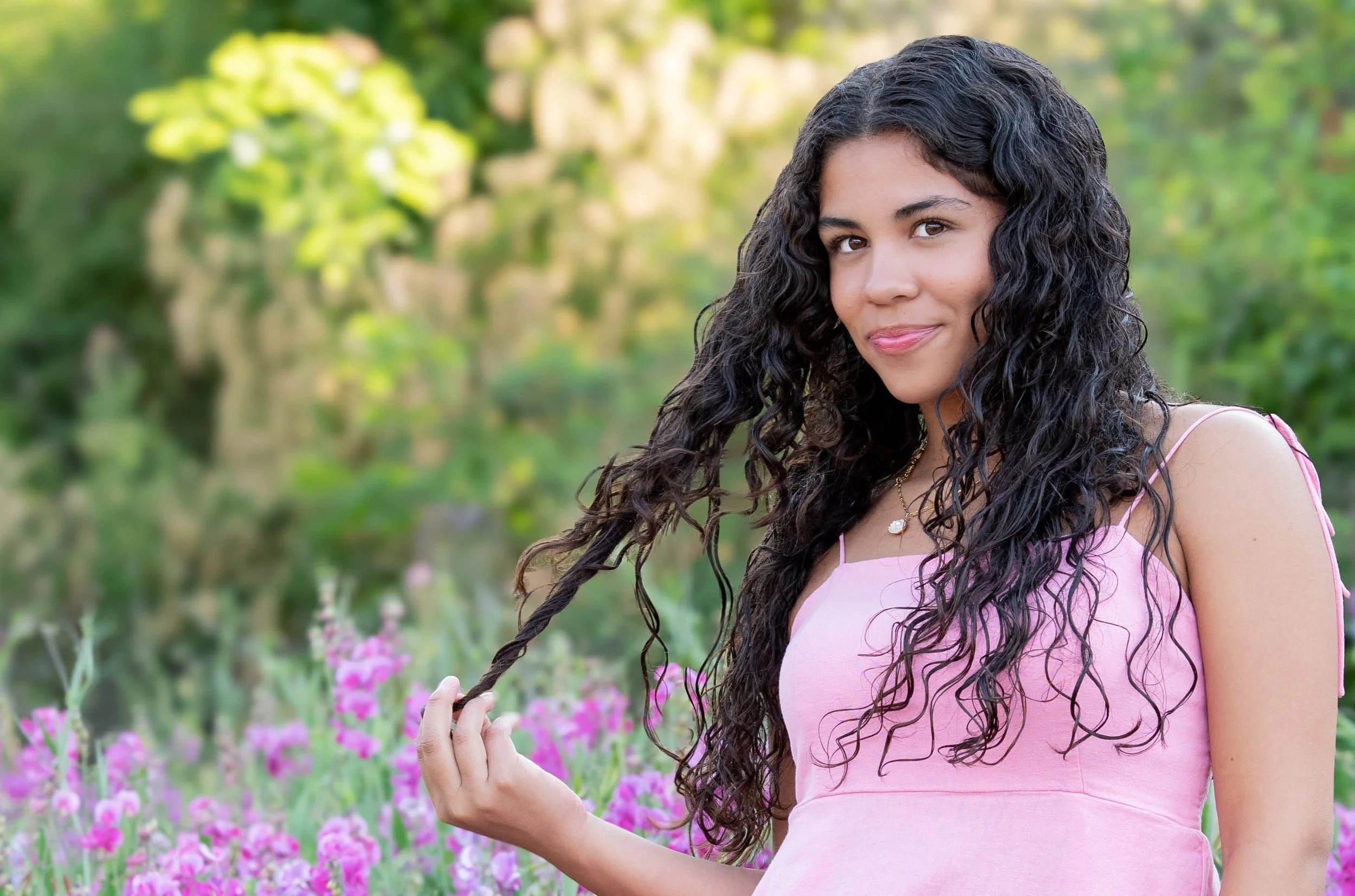 Senior High School photoshoot, standing among pink flowers in a garden with greenery in the background. Portland OR