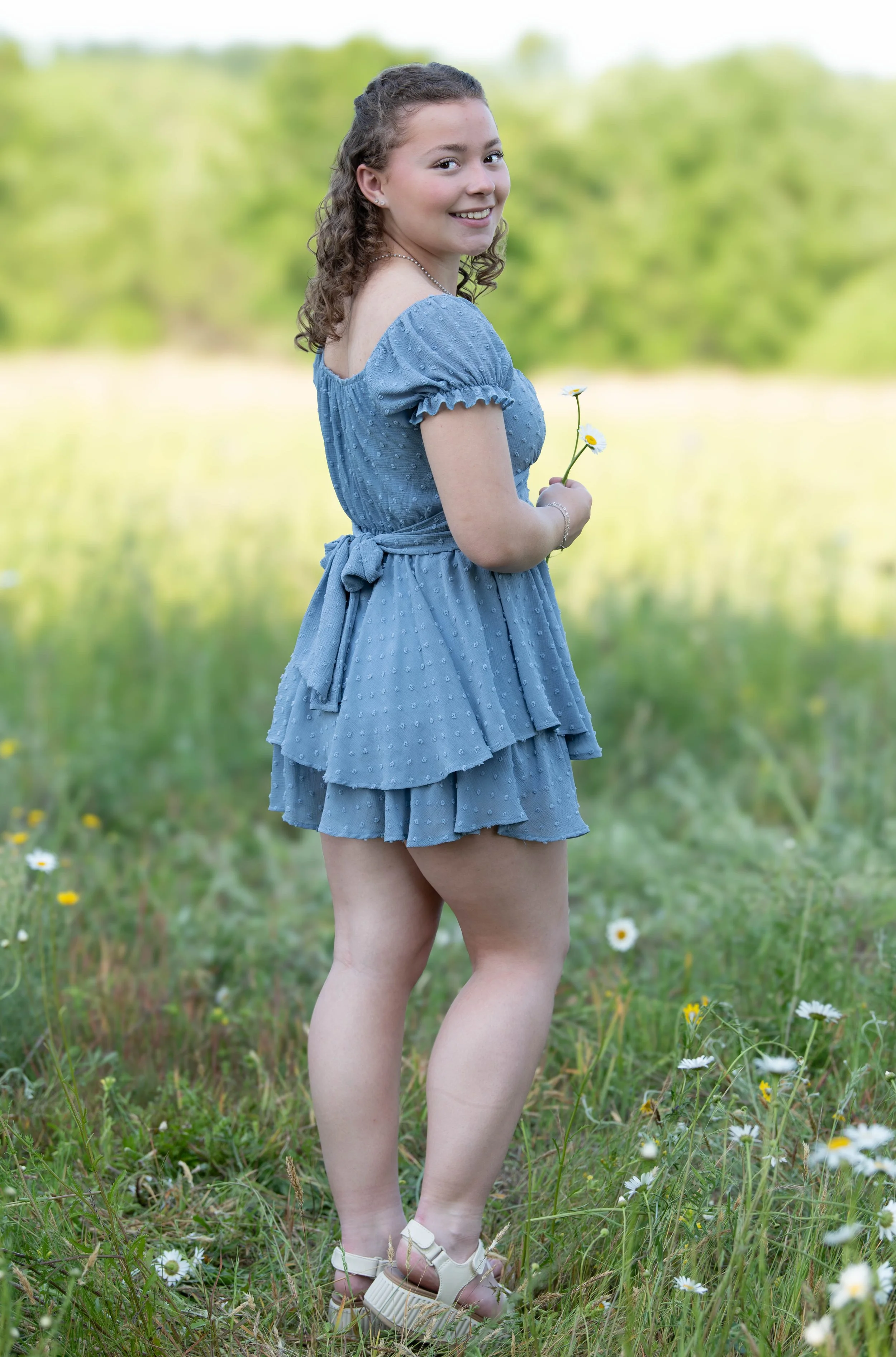 Senior High School Photoshoot, standing outdoors in a grassy field with flowers and green trees in the background. PDX