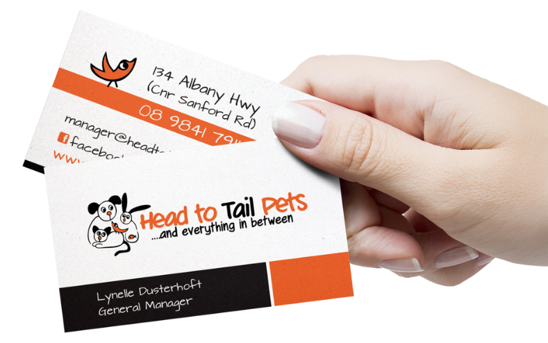 Close-up of a hand holding a business card for Head to Tail Pets, featuring a cartoon dog and cat, with contact details and the slogan '..and everything in between'.