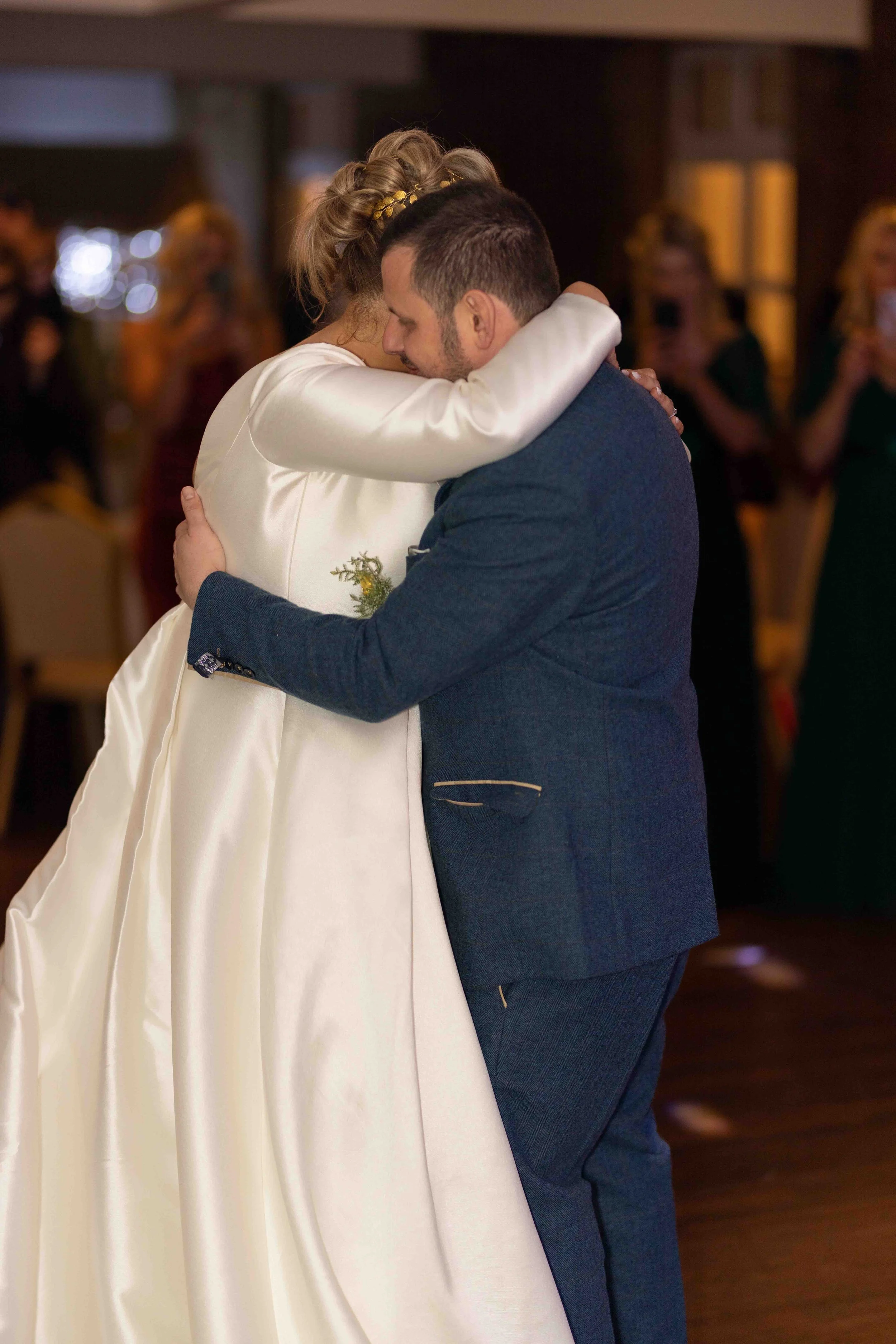 A bride in a white wedding dress and a groom in a dark suit embrace during their wedding reception.