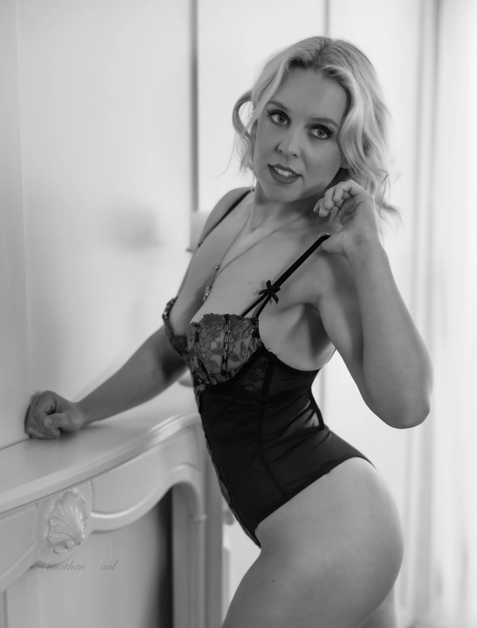 Black and white photo of a woman in lingerie posing indoors.