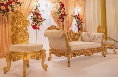 Elegant living room with golden ornate furniture, floral arrangements, and soft, beige drapes.