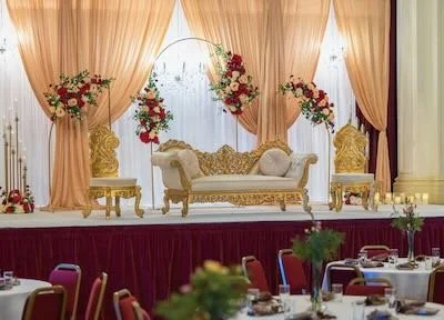 Elegant stage decorated with peach and gold curtains, floral arrangements, and a gold and white sofa set for a wedding or event.