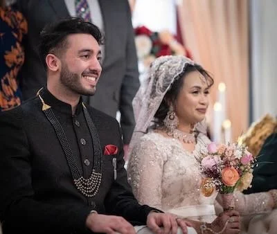 A groom and bride smiling during a wedding ceremony, with the bride holding a bouquet of flowers.
