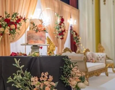 Decorated event space with a wedding cake on a stand, floral arrangements, and vintage furniture.