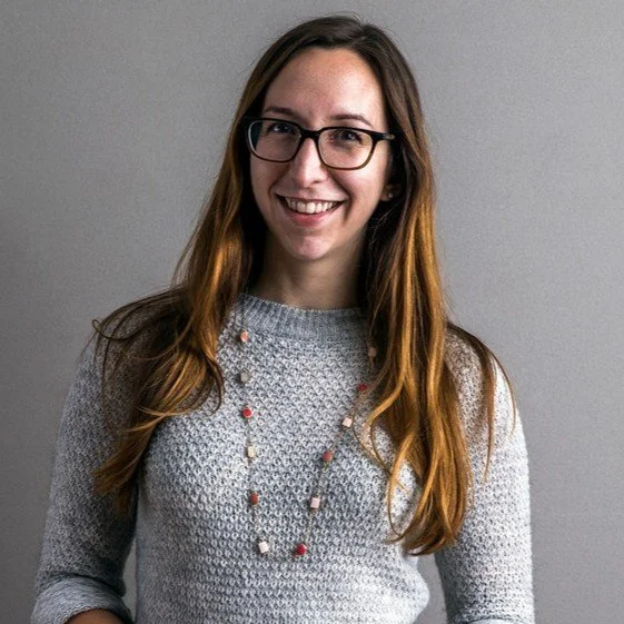professional headshot of a woman with long brown hair wearing glasses and a gray sweater