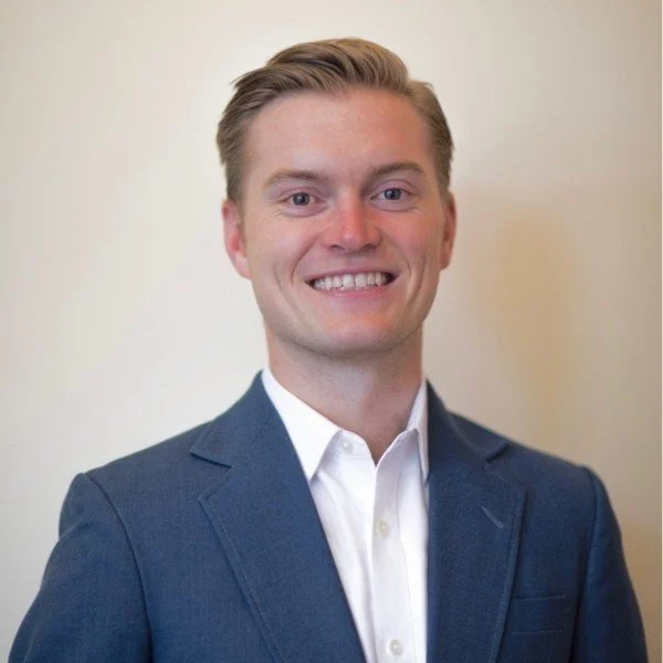 professional headshot of a smiling man with short blonde hair, a crisp white button down and blue suit jacket