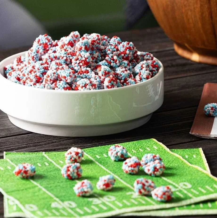 Huge Galdones photograph for Ferrara Candy Nerds Gummy Clusters bowl of red, white, and blue speckled candy balls on a dark wooden surface, with some candy balls on a green napkin designed like a football field.