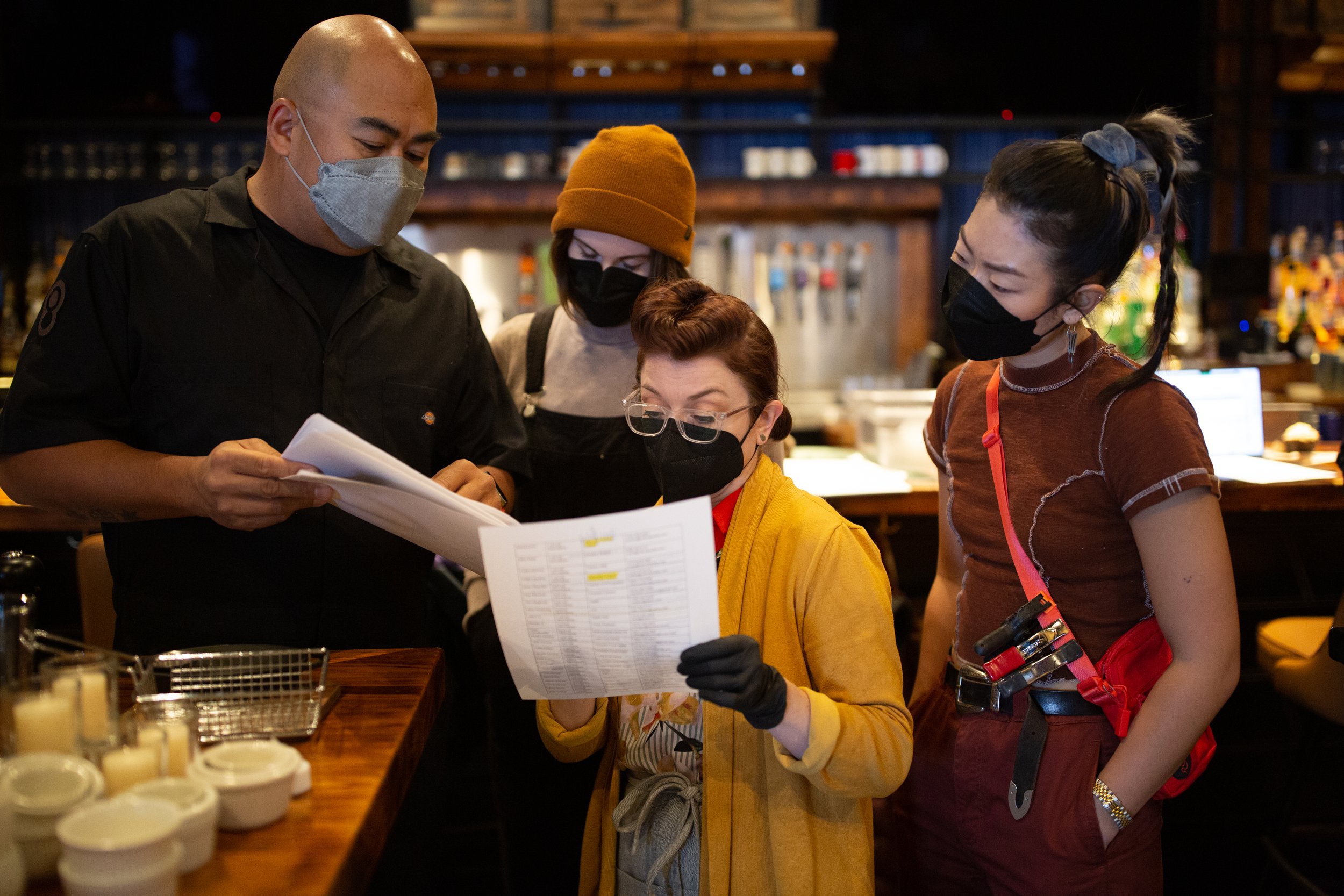 Four people wearing face masks in a restaurant setting reviewing documents.