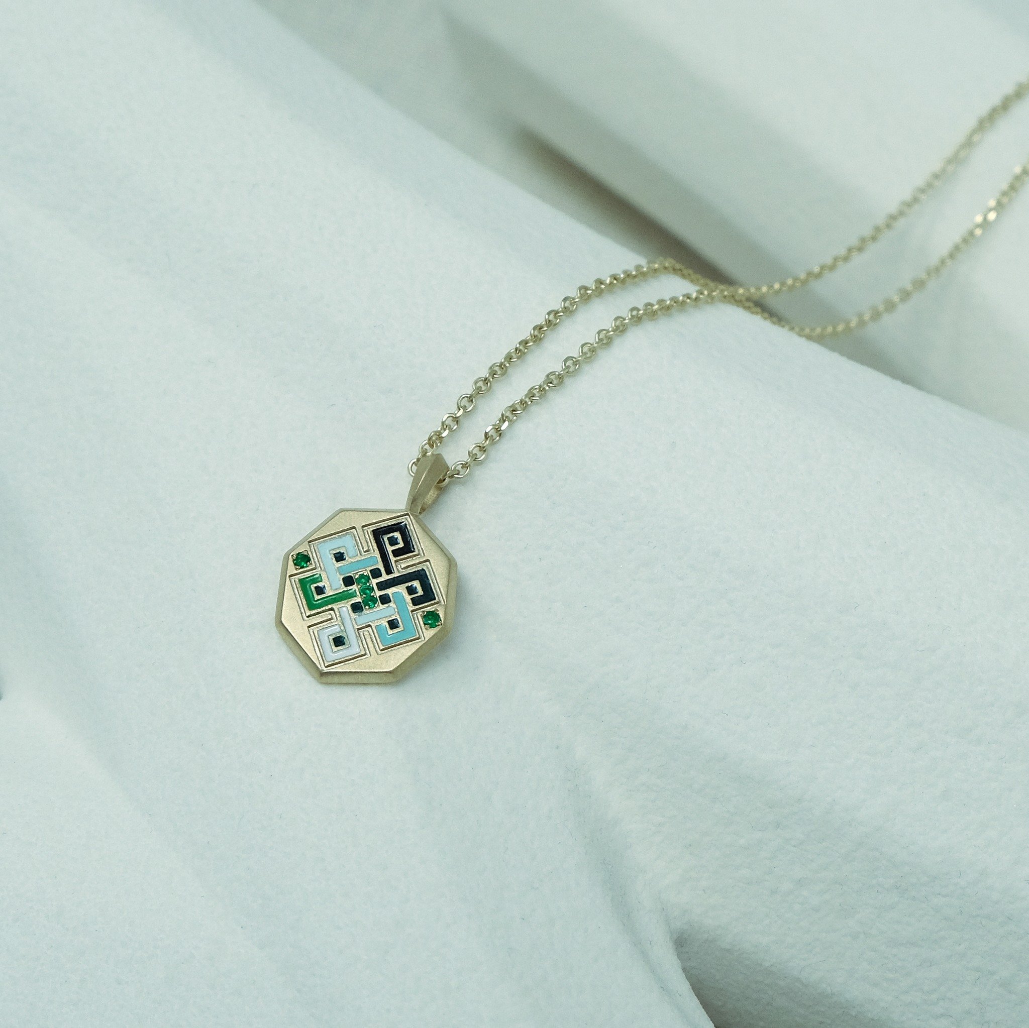 A faceted hexagon beauty in matte finished yellow gold with multi-colour enamel with round brilliant-cut Indian emeralds.
.
The pendant features an endless knot pattern, symbolising wisdom and compassion. It is one of the eight auspicious symbols, an