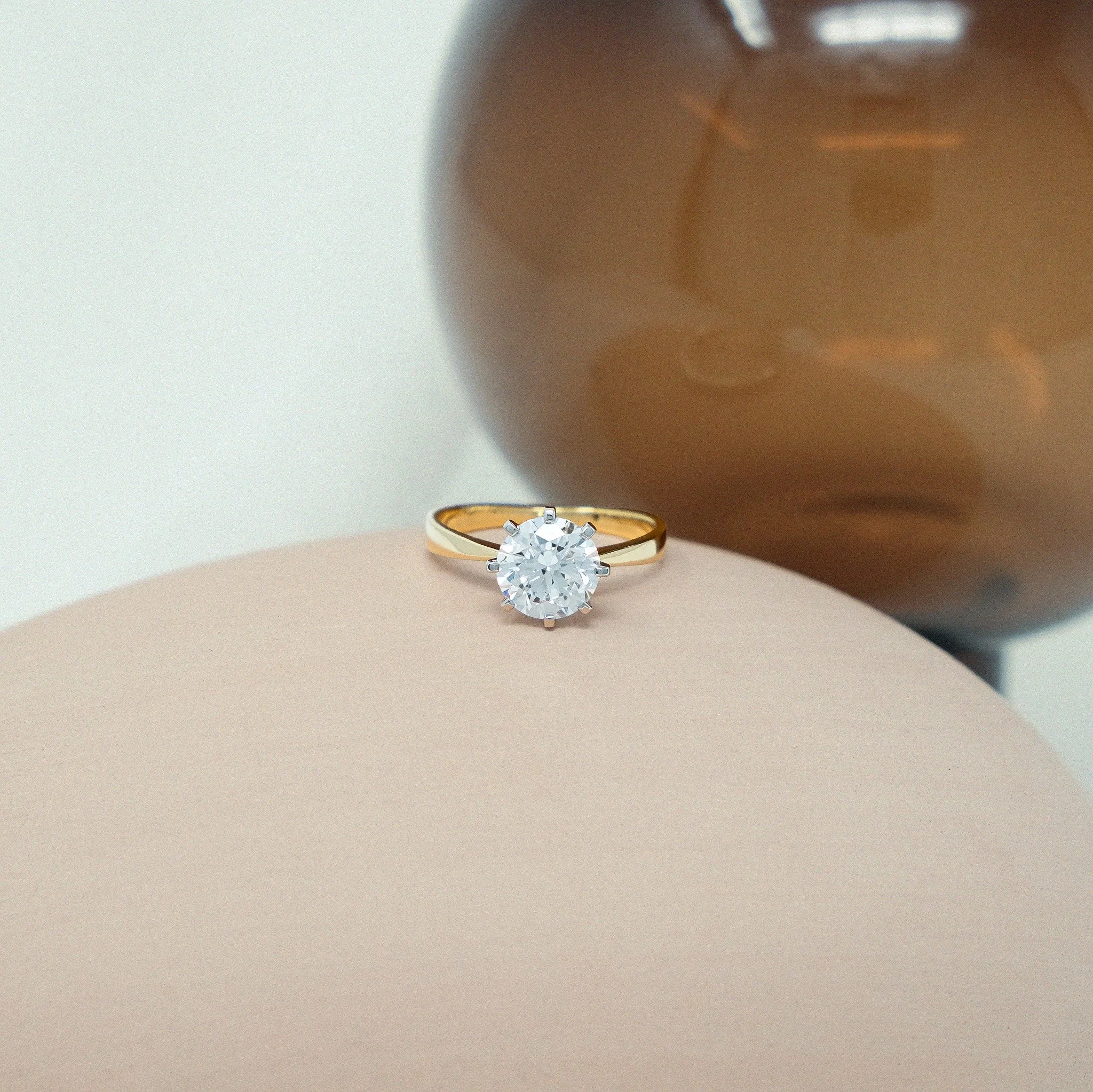 A study in proportion, contrast, and quiet strength &mdash; the Adrila Ring. Meticulously handcrafted in 18ct yellow gold and platinum, this design centres around a luminous 2.10ct round brilliant-cut white diamond. The diamond is held in a square pl