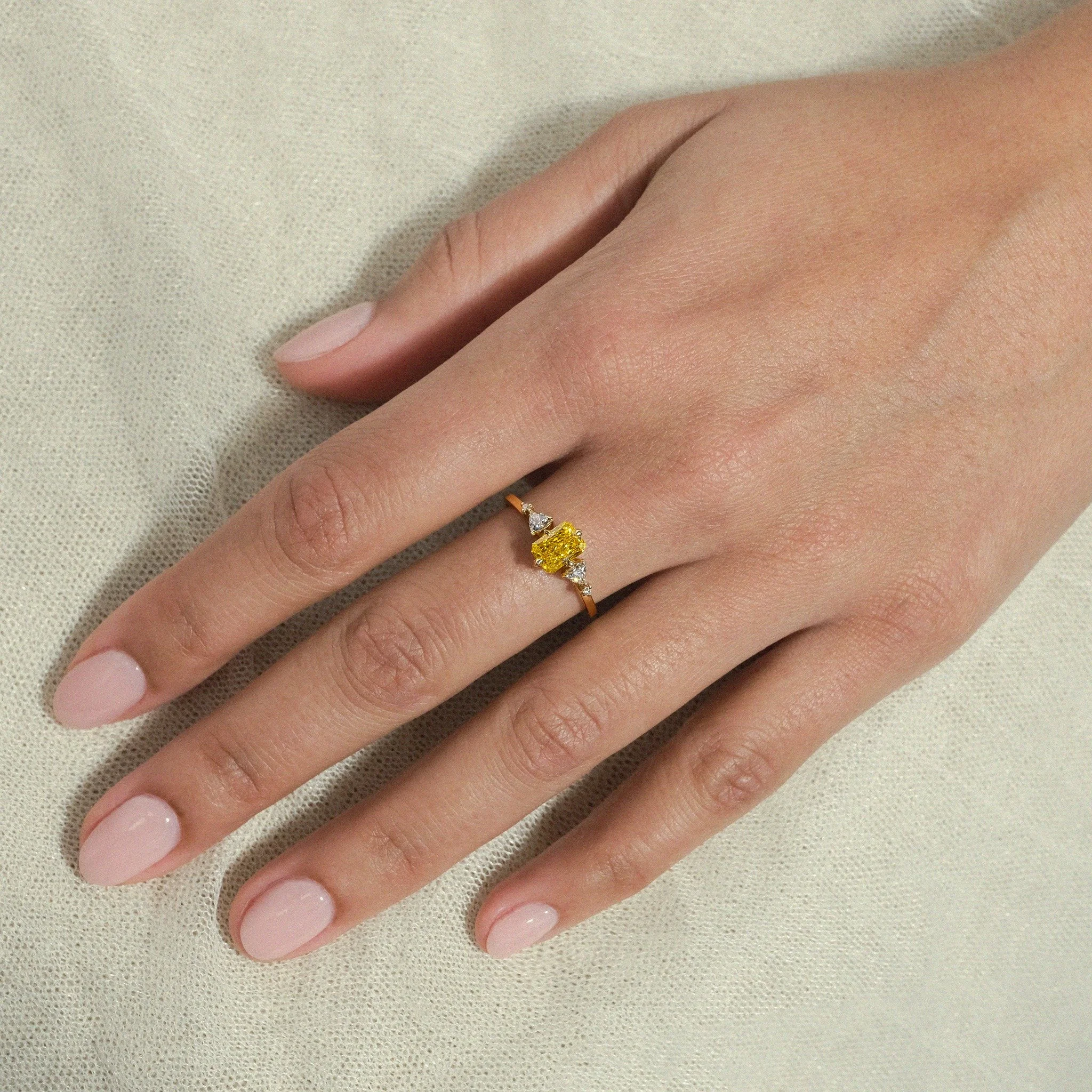 Golden light, captured forever. The Amara Ring celebrates the beauty of bold elegance through a radiant-cut yellow diamond, framed by a harmonious composition of trillion and round brilliant white diamonds. Clean lines, sculptural proportions, and an