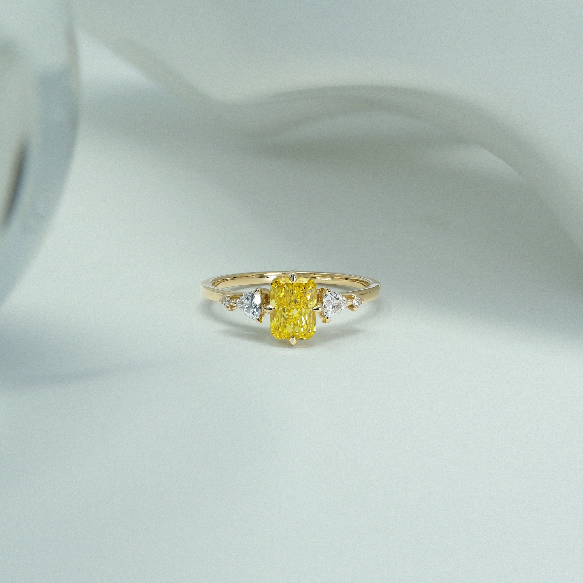 Golden light, captured forever.

The Amara Ring pairs the electric warmth of a radiant-cut yellow diamond with crisp trillion and round brilliant accents. With its sculptural lines, architectural tiger claws, and vintage Art Deco soul, it bridges con