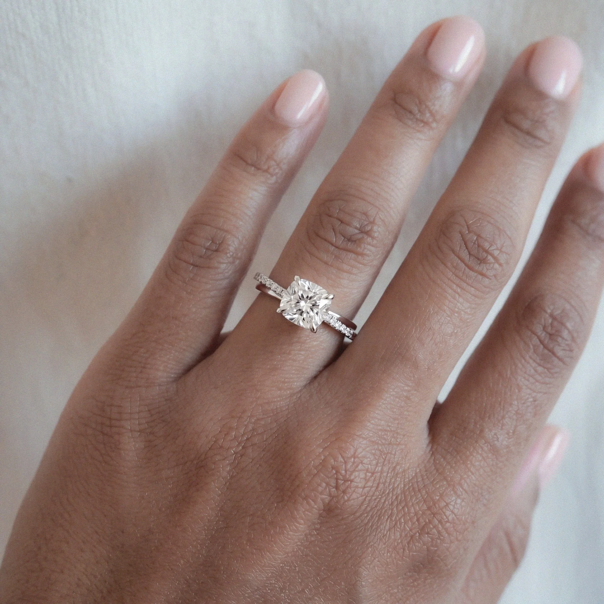 Aelia modern engagement ring in platinum with cushion-cut white diamond and small diamond pave from EDXU bespoke jeweller London on a model hand