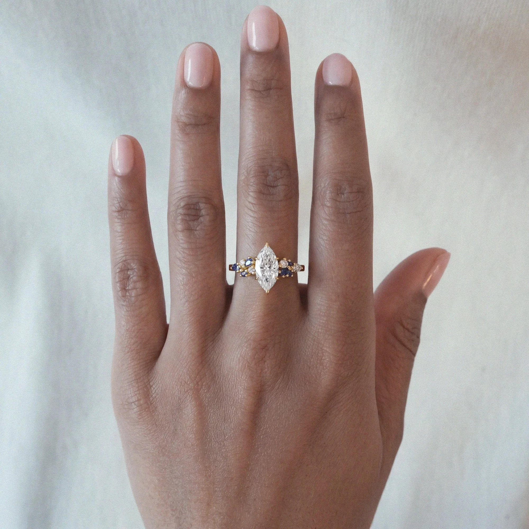Celeste alternative engagement ring in 18ct yellow gold with marquise-cut white diamond and small sapphires and diamonds side stones from EDXU bespoke jeweller London on model hand