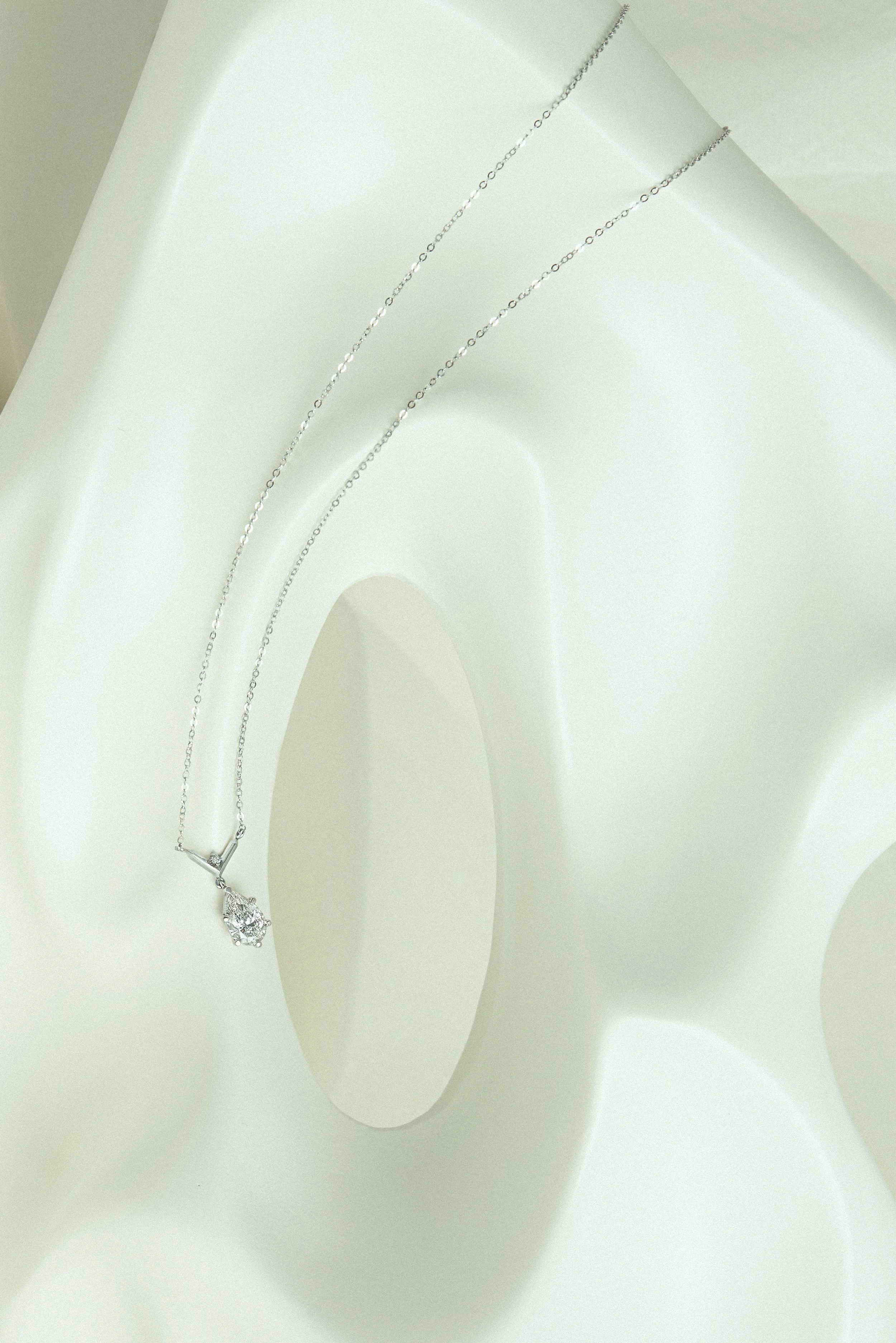 bespoke 18k white gold necklace with pear-cut and round brilliant-cut white diamond sitting on top of abstract vase EDXU London campaign