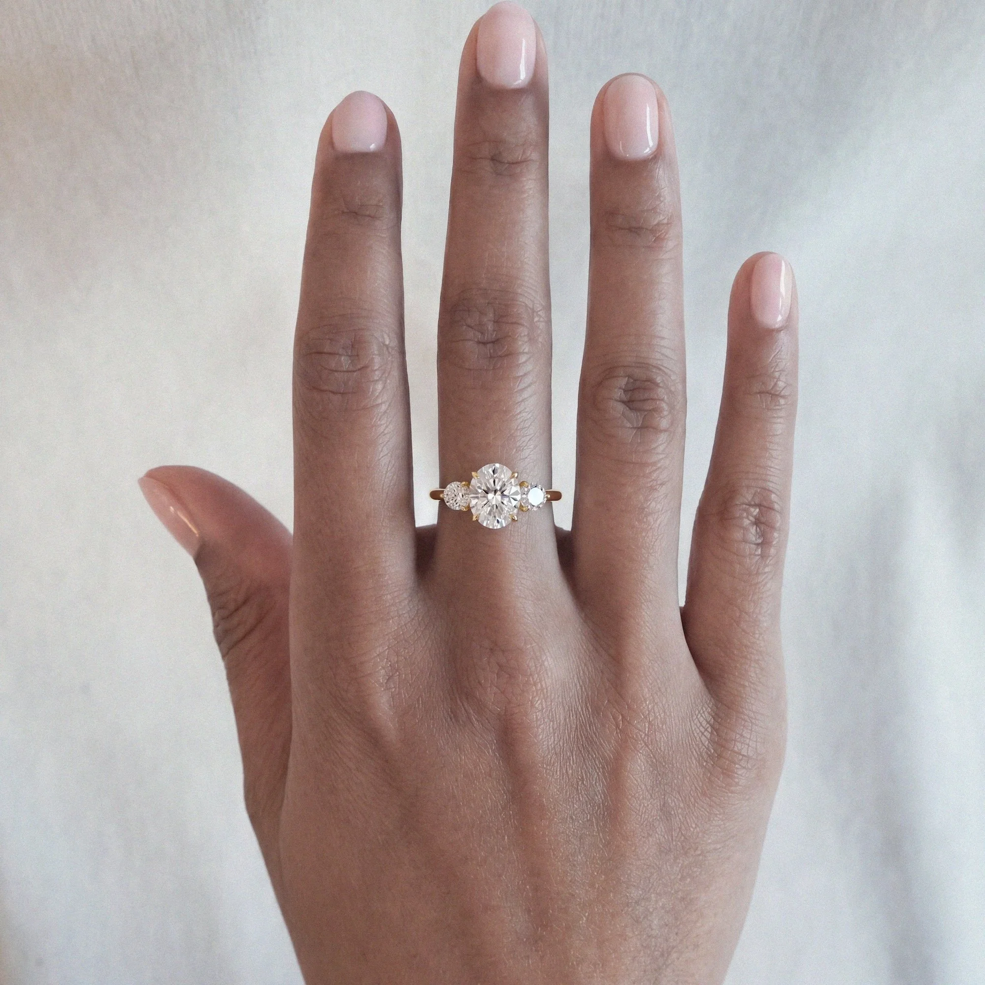 Clara modern engagement ring in 18ct yellow gold with oval-cut diamond and 2 round diamonds on shoulders from EDXU bespoke jewellery London editorial