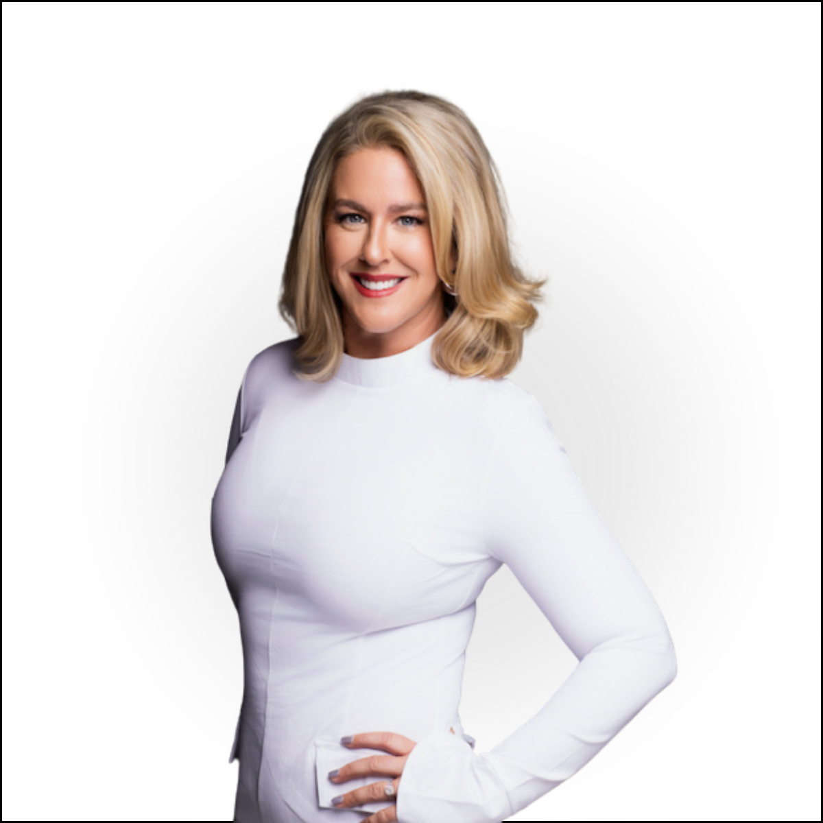 A smiling woman with blonde hair in a white long-sleeve top, standing with her hand on her hip against a plain white background.