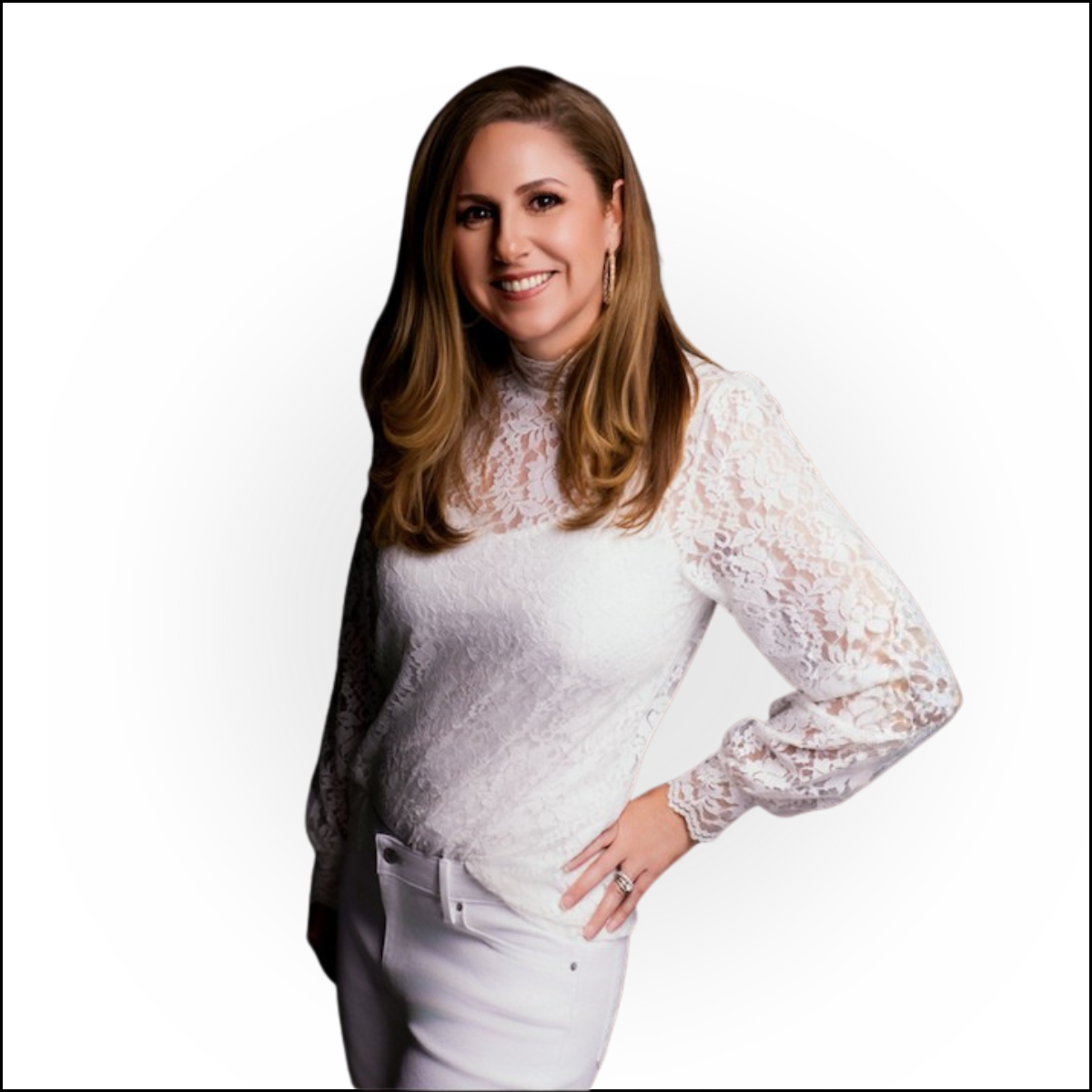 A woman with long, wavy light brown hair, smiling, wearing a white lace long-sleeve top and white pants, posing with her hand on her hip against a plain white background.