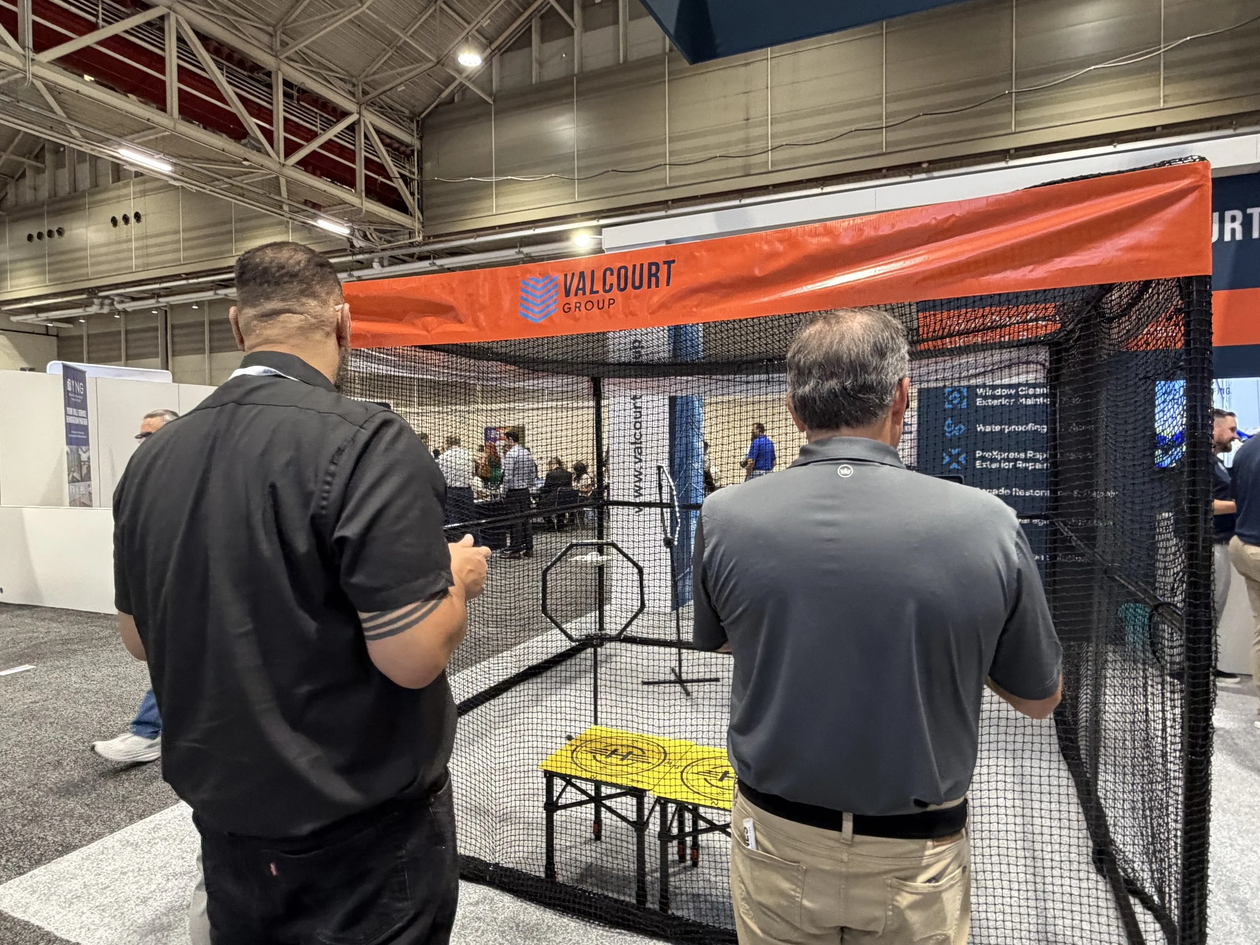Attendees watching a mini-drone race inside a netted course at a trade show booth
