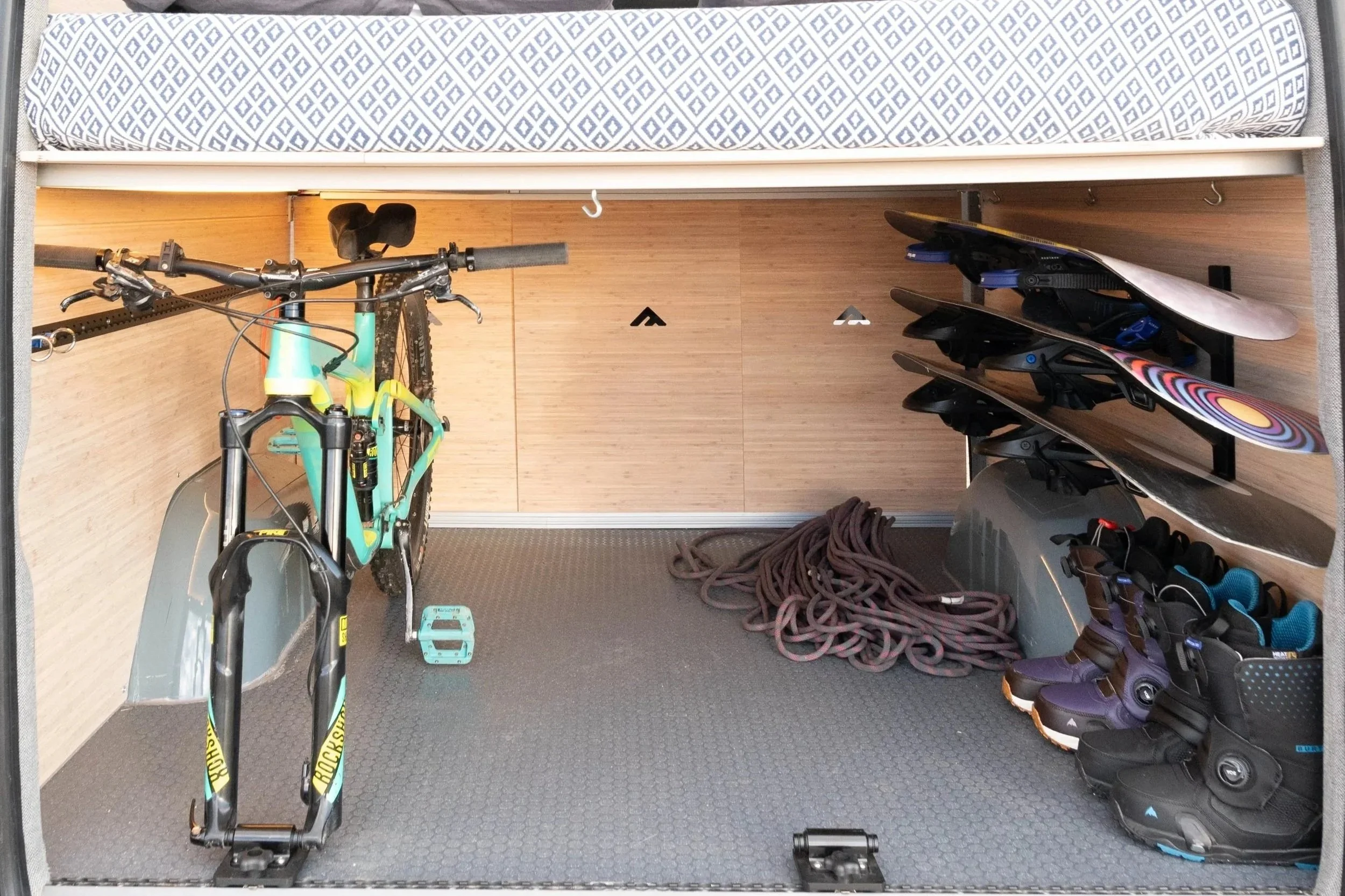 Inside of a garage with a mountain bike, skateboards, climbing shoes, and a coiled climbing rope.