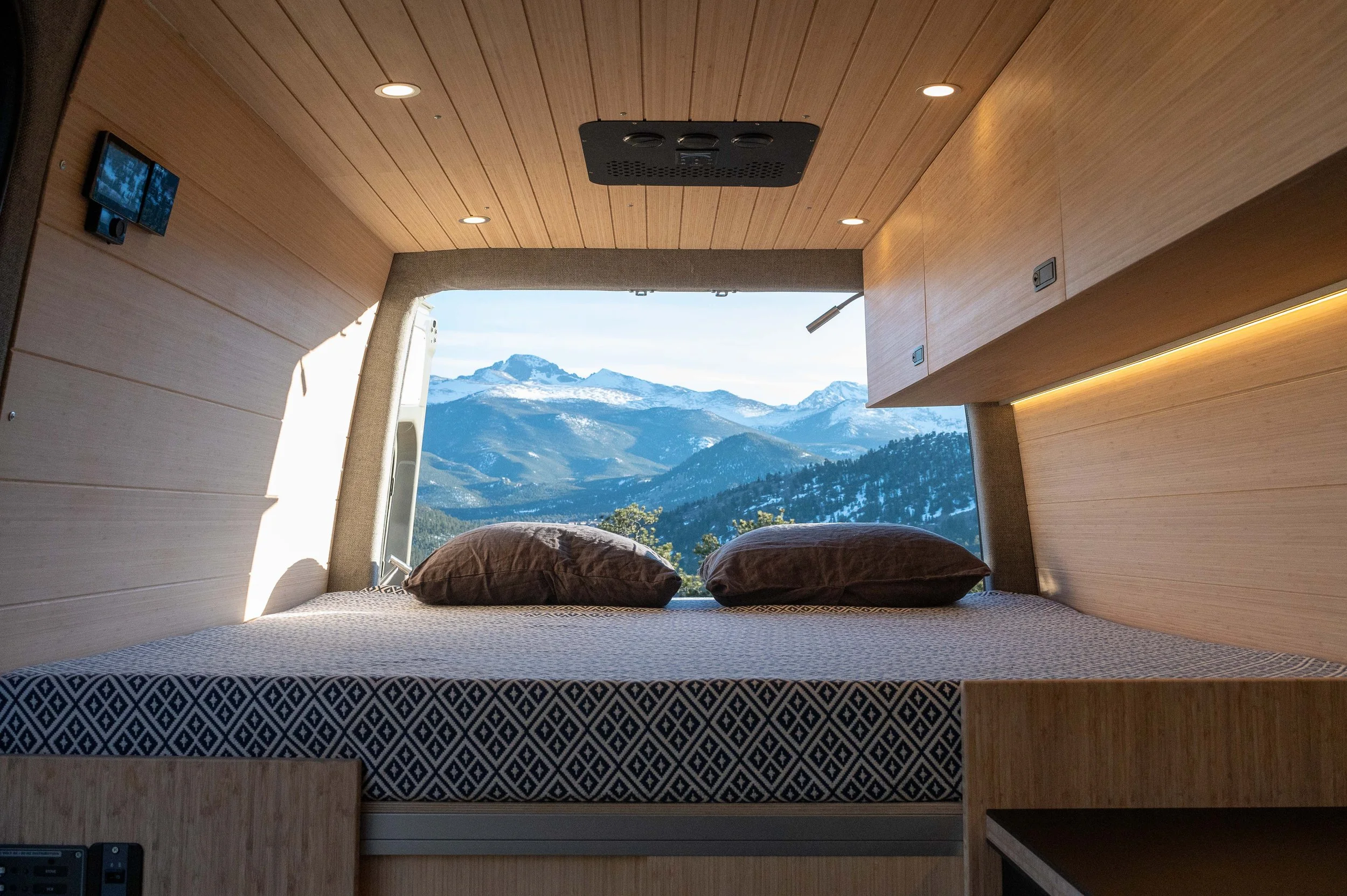 A bedroom with a large window showcasing a mountain landscape with snow-capped peaks and forests.