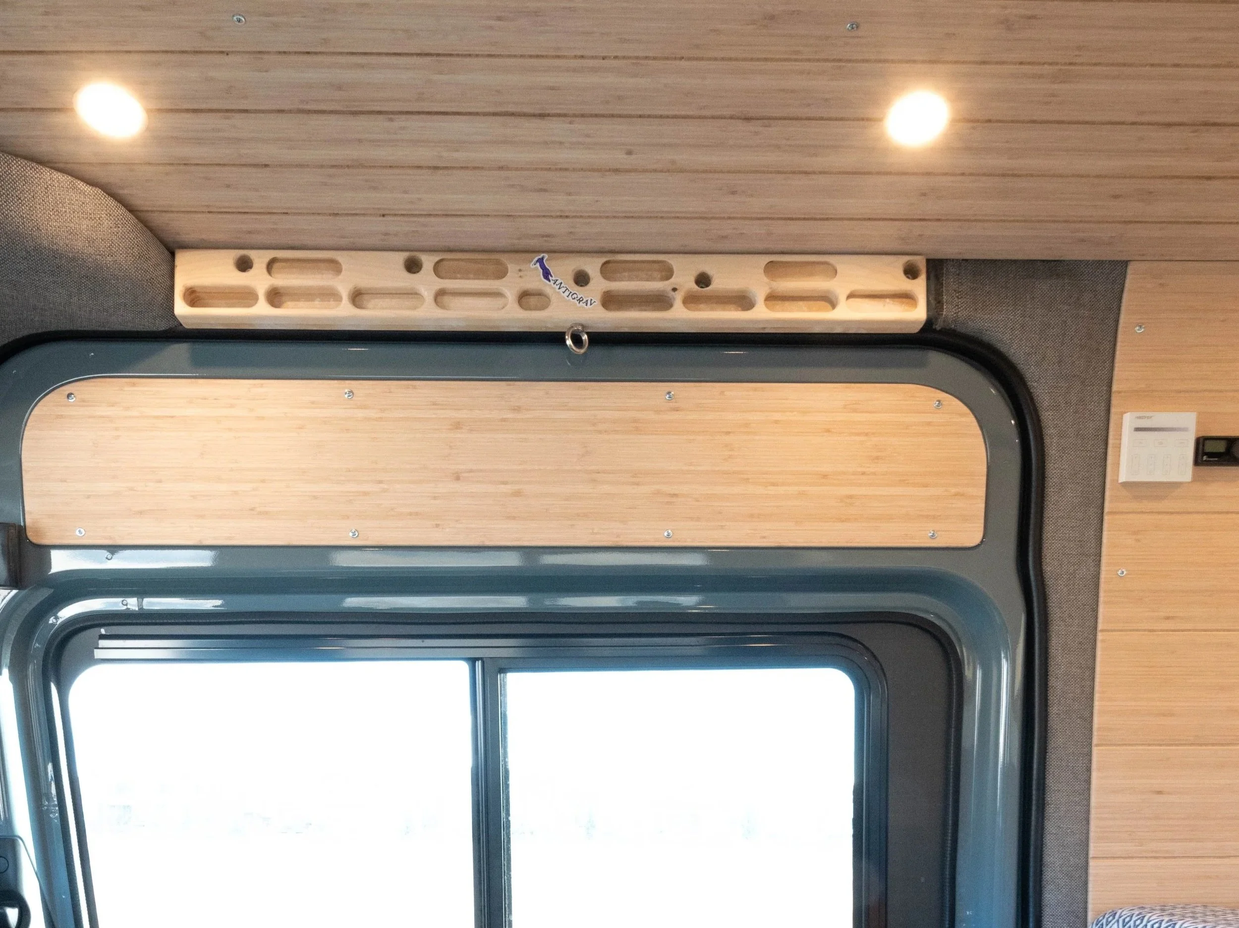 Interior view of a vehicle's ceiling showing a wooden panel, a metal frame, and a wooden shelf with a small purple sticker labeled 'Antitogray'.