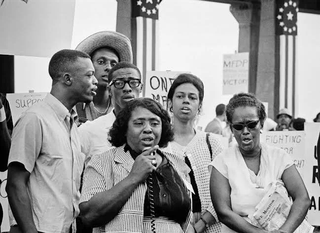 MFDP founders Fannie Lou Hamer (c) and Ella Baker (far right) and delegates, (far left to right rear) Emory Harris, Stokely Carmichael (straw hat), Sam Block and Eleanor Holmes Norton sing on the Boardwalk during the Democratic National Convention.
