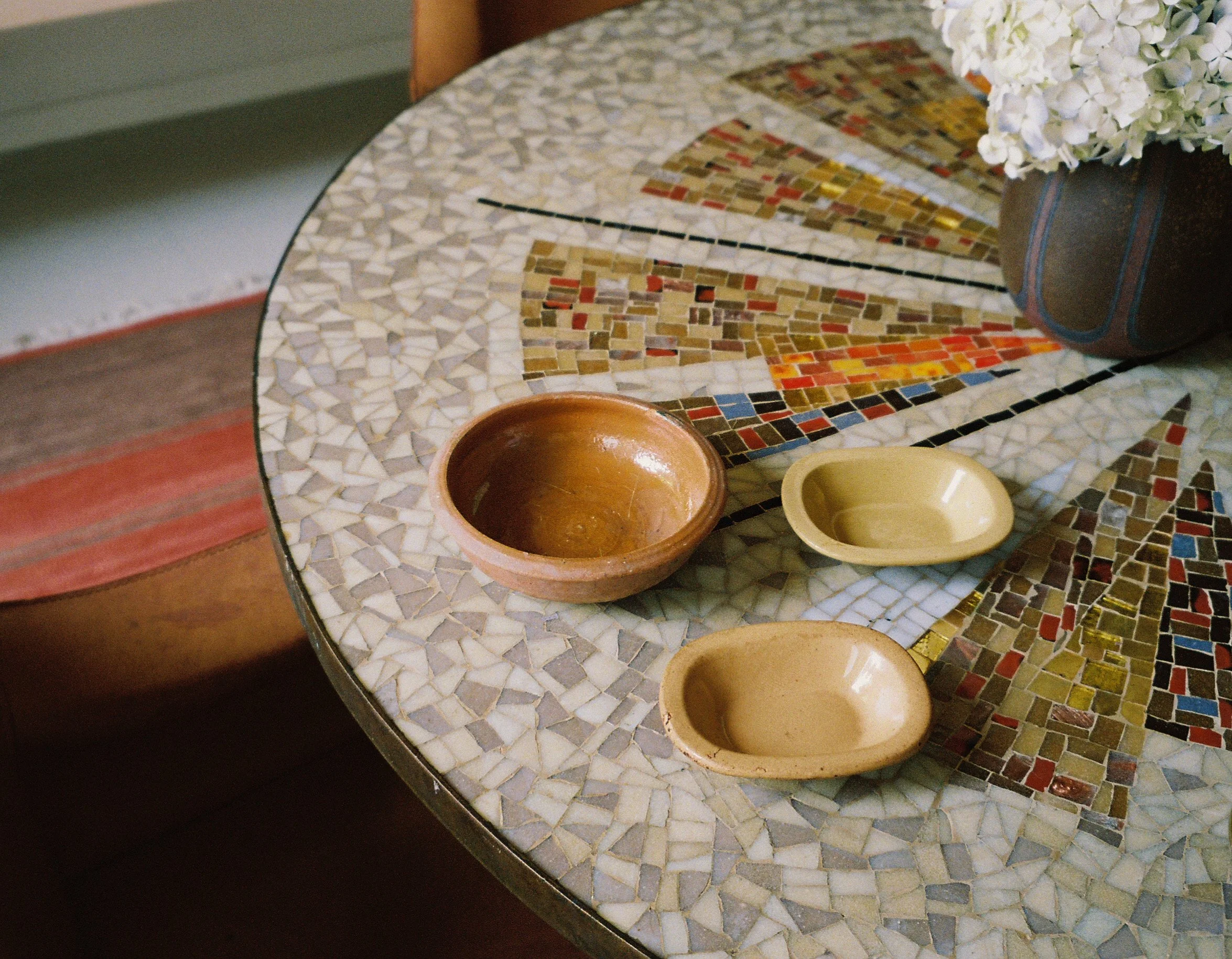 Round mosaic table with several small ceramic bowls and a vase of white flowers.