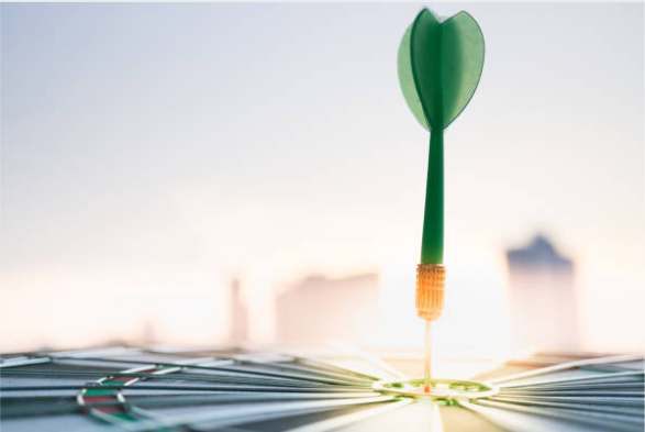 Green dart stuck in a dartboard bullseye with a blurred city skyline in the background.
