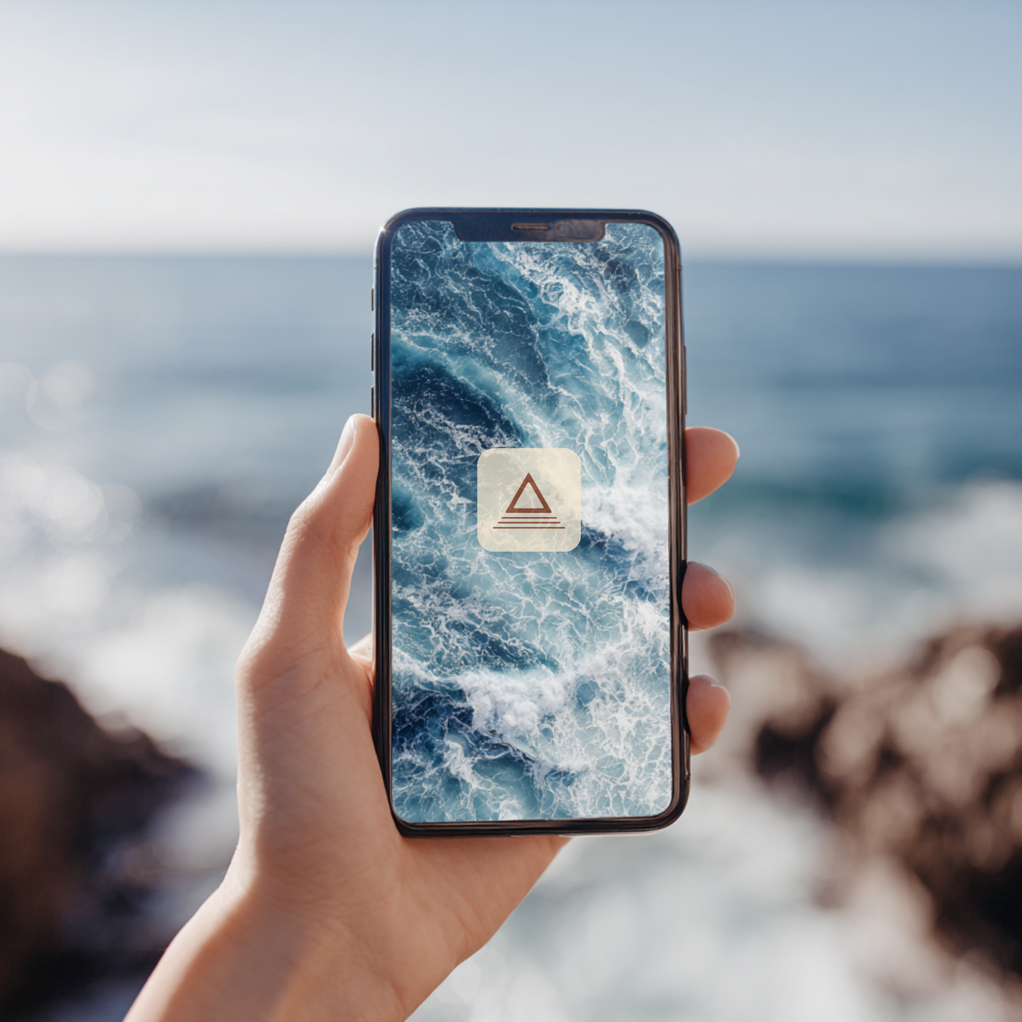 Person holding a smartphone with a wave pattern on the screen, outdoors near the ocean.