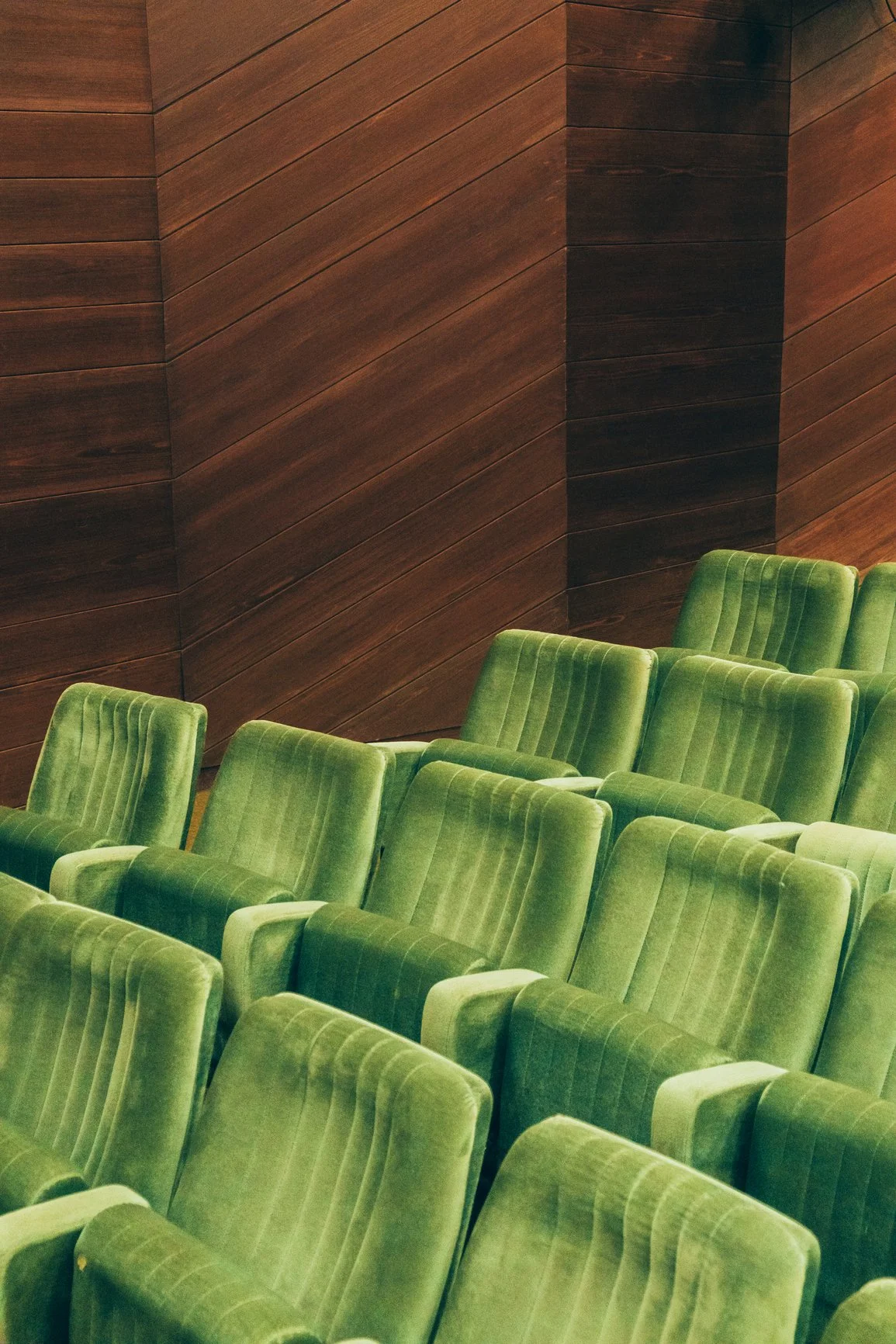 Several green velvet seats arranged in rows against a wooden-paneled wall, with a slight angle view.