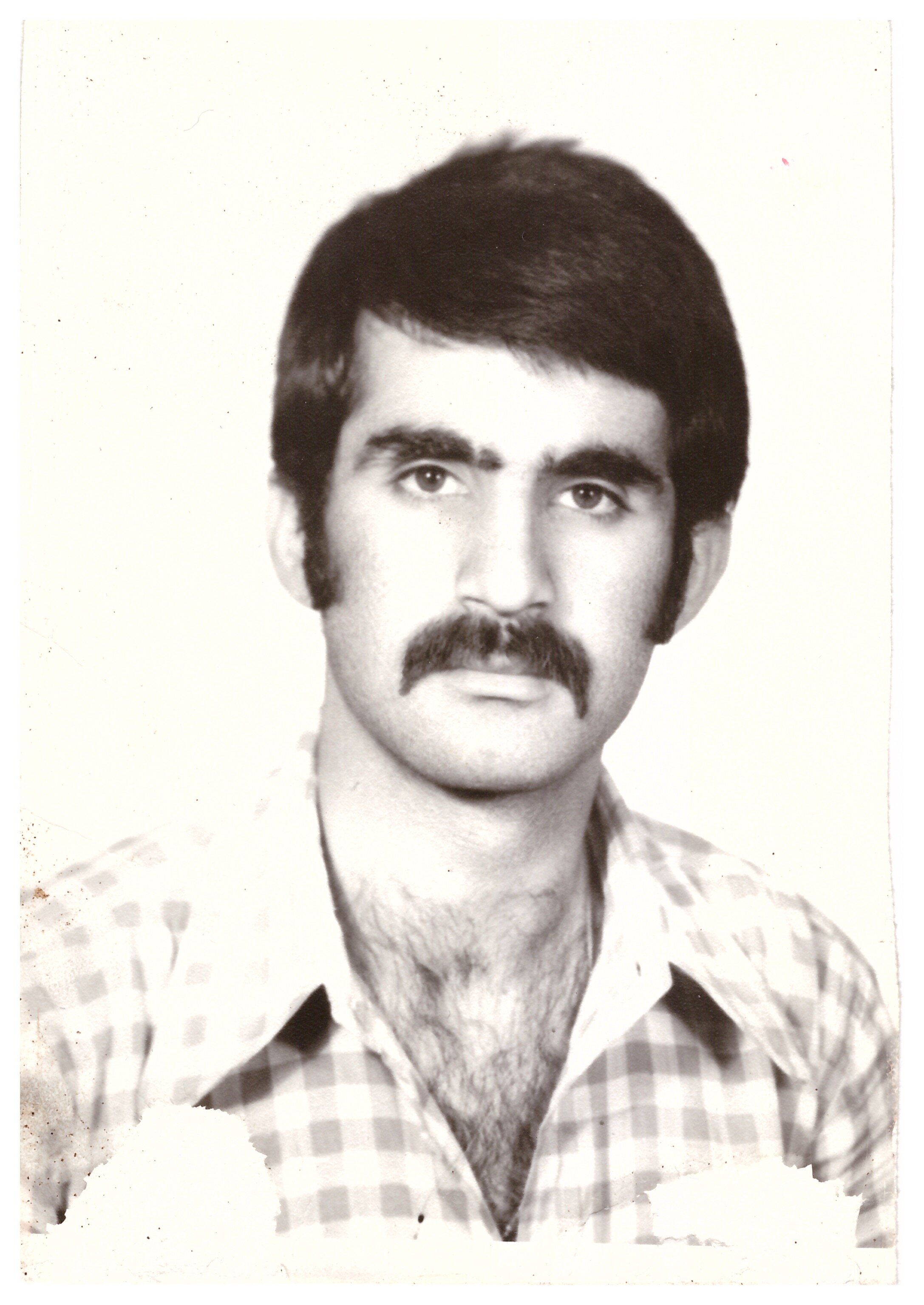 Black and white photo of a man with dark hair and a mustache wearing a plaid shirt, possibly from the 1970s.