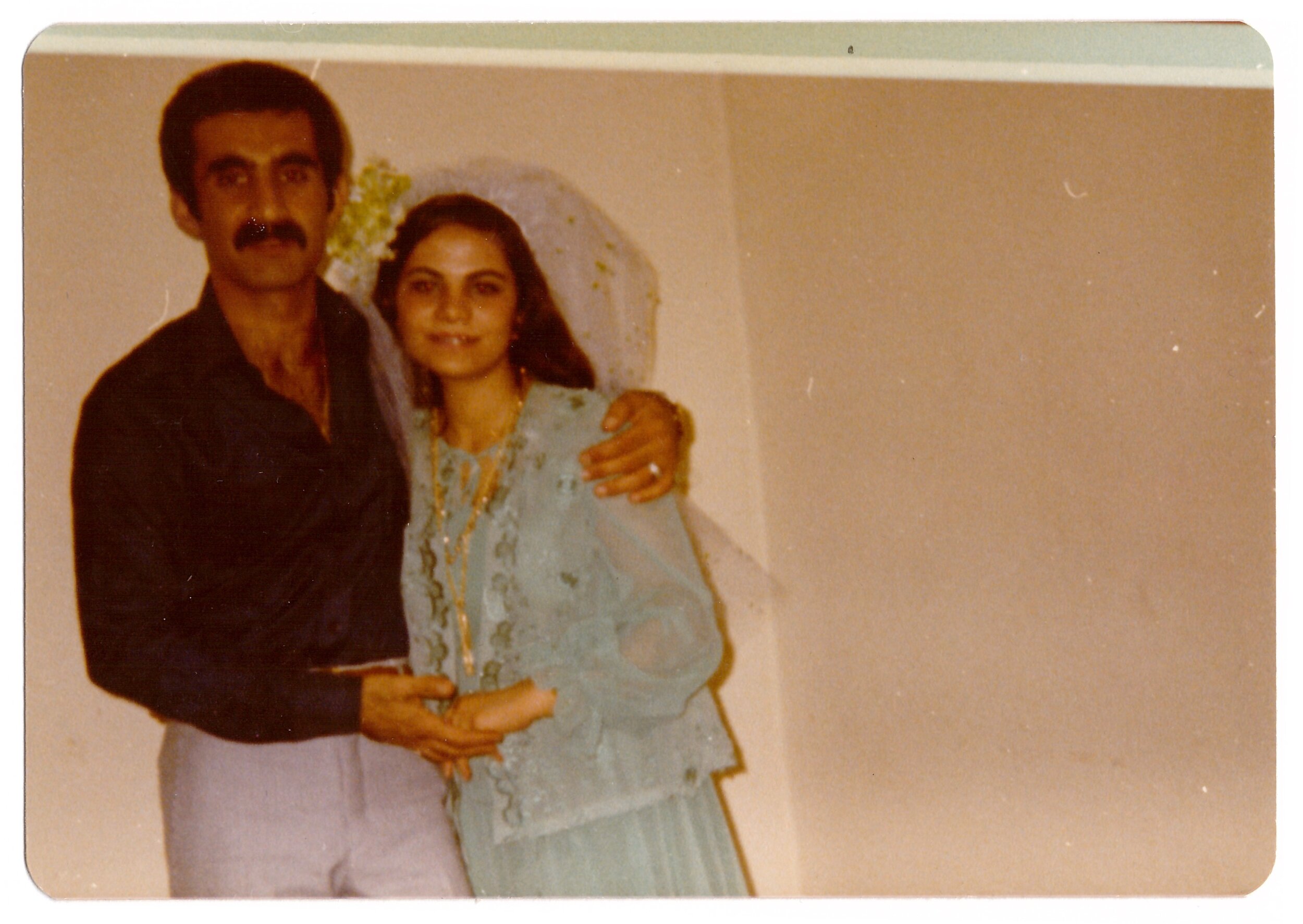 A man and woman posing in formal attire, with the woman wearing a garment with lace and a veil.