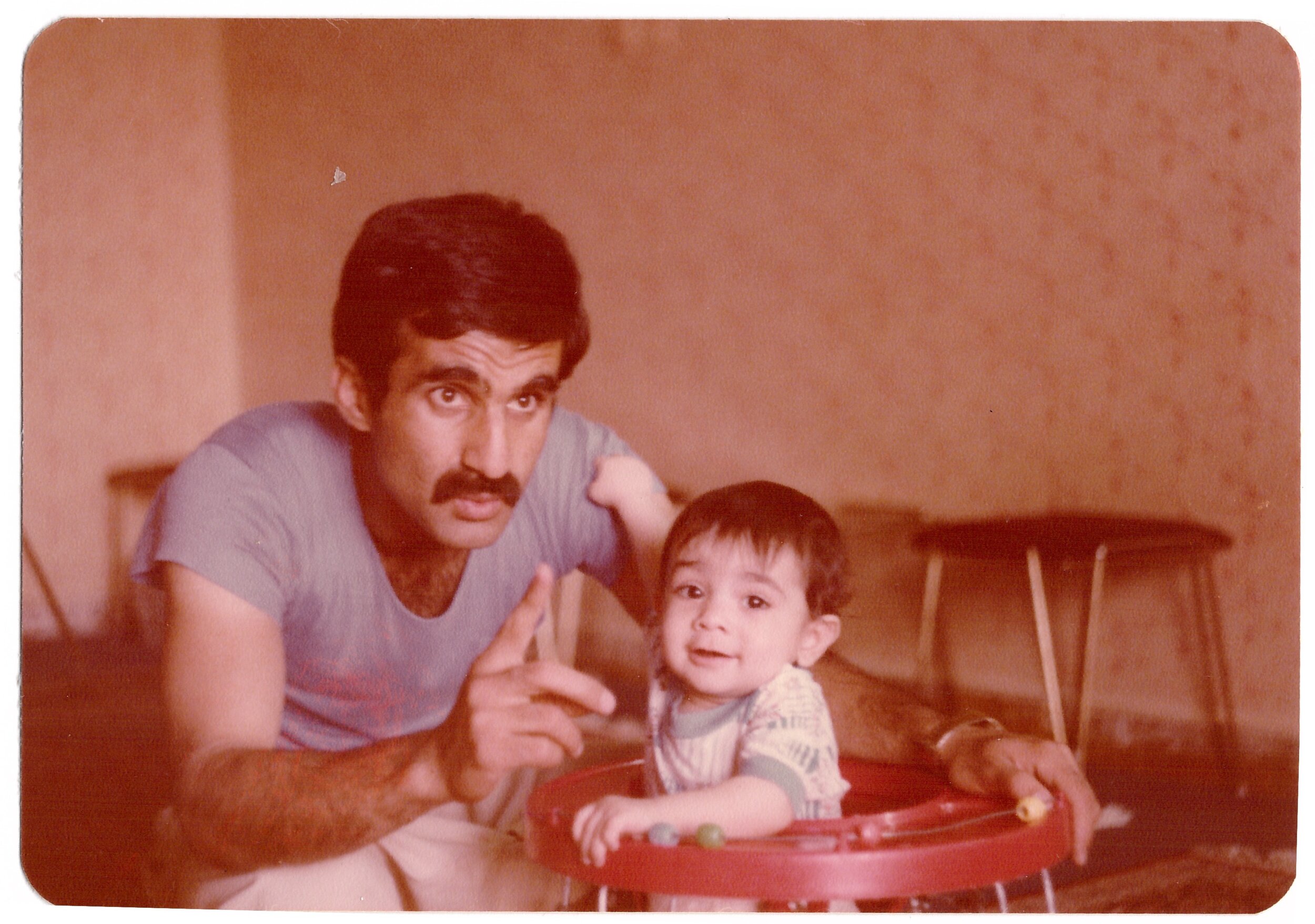 Man with mustache and baby in a walker indoors
