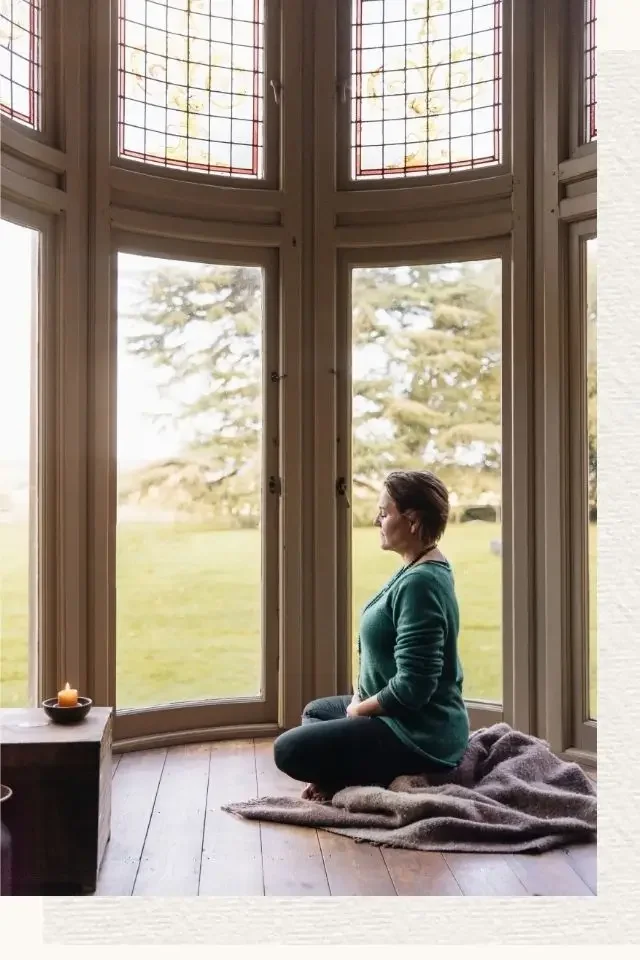 Karin Peeters meditating in front of a stunning window