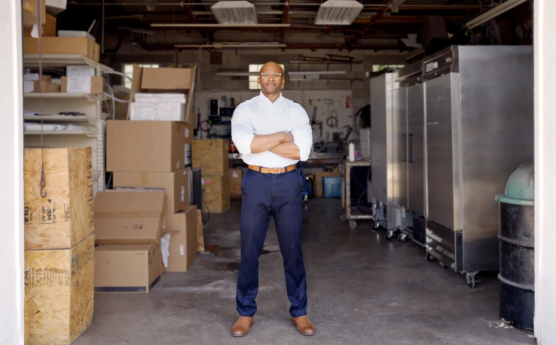 A man standing arms-crossed in a parts warehouse — Teamshares employee-owner portrait (CRH).