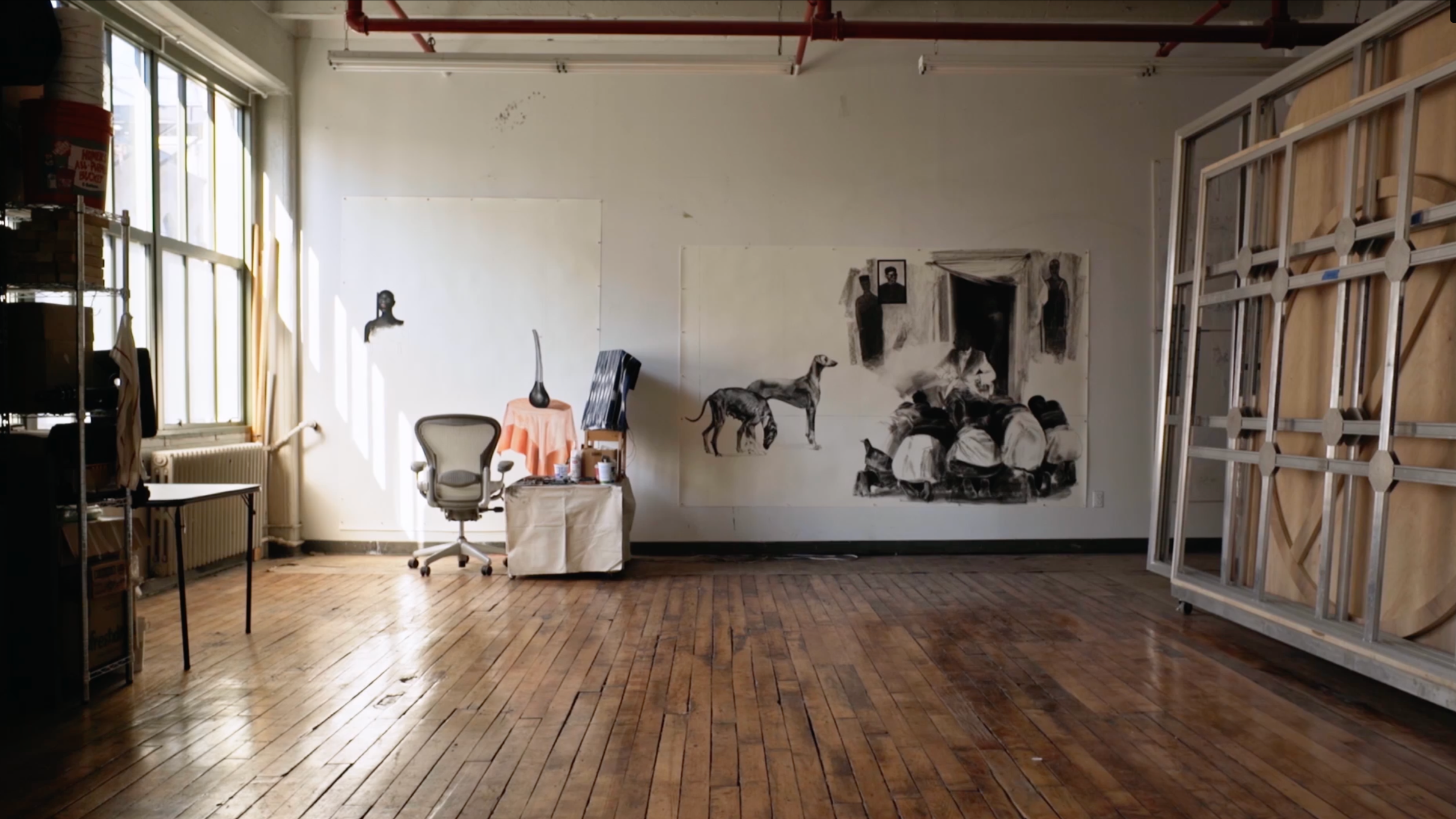 Artist Meleko Mokgosi's studio, hung with large figurative paintings, wood floor and work chair — THEY documentary work.