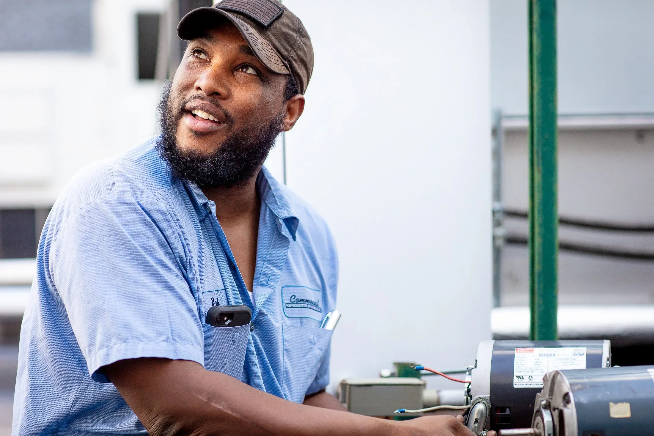 A bearded worker in a cap and blue shirt repairing a rooftop HVAC unit — Teamshares documentary still for CRH.