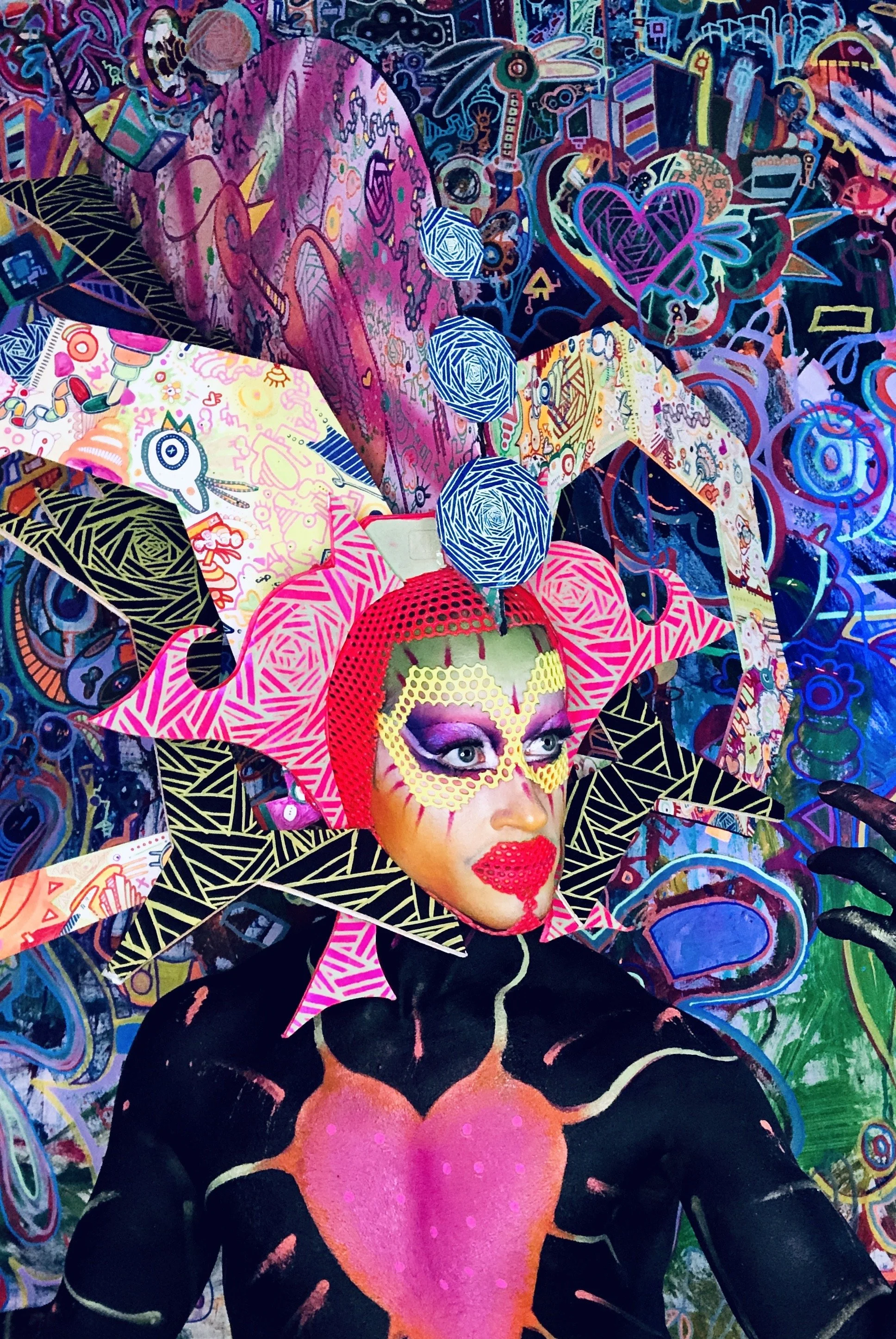 A person with elaborate, colorful makeup and costume inspired by pop art and surrealism, surrounded by a vibrant, graffiti-style mural with hearts, faces, and abstract designs