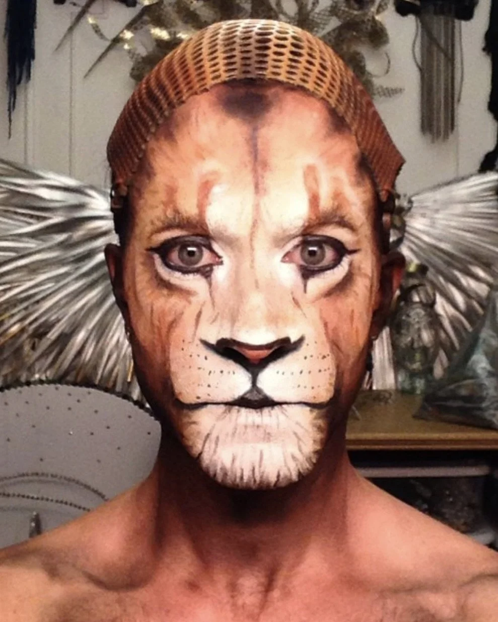 A person with face makeup and a costume resembling a lion, including a painted lion face on their face and a lion mane and ears as a headpiece.