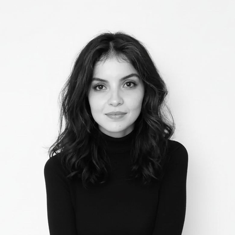Black and white portrait of a young woman with wavy, shoulder-length hair, wearing a black turtleneck, smiling slightly, against a plain white background.
