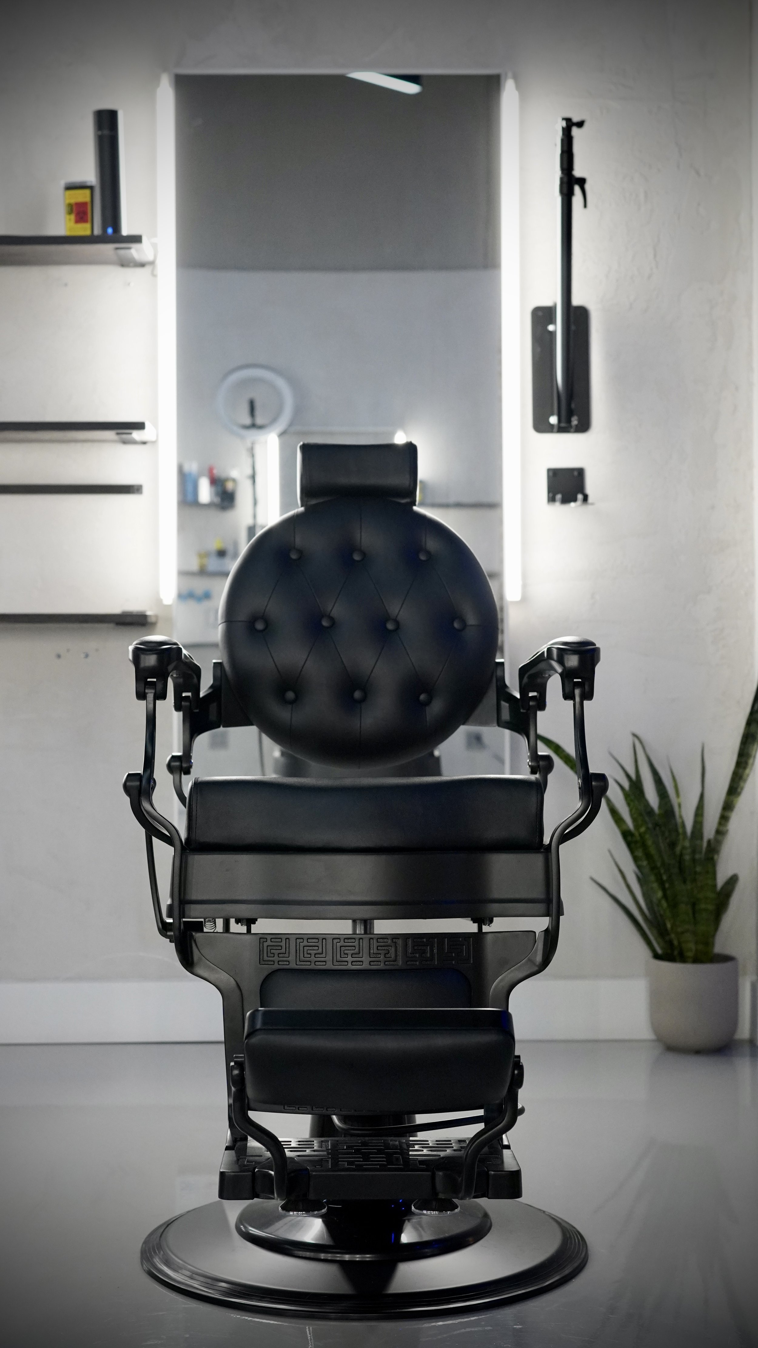 Barber's chair in a modern barbershop, facing a mirror, with a plant in a pot to the right.
