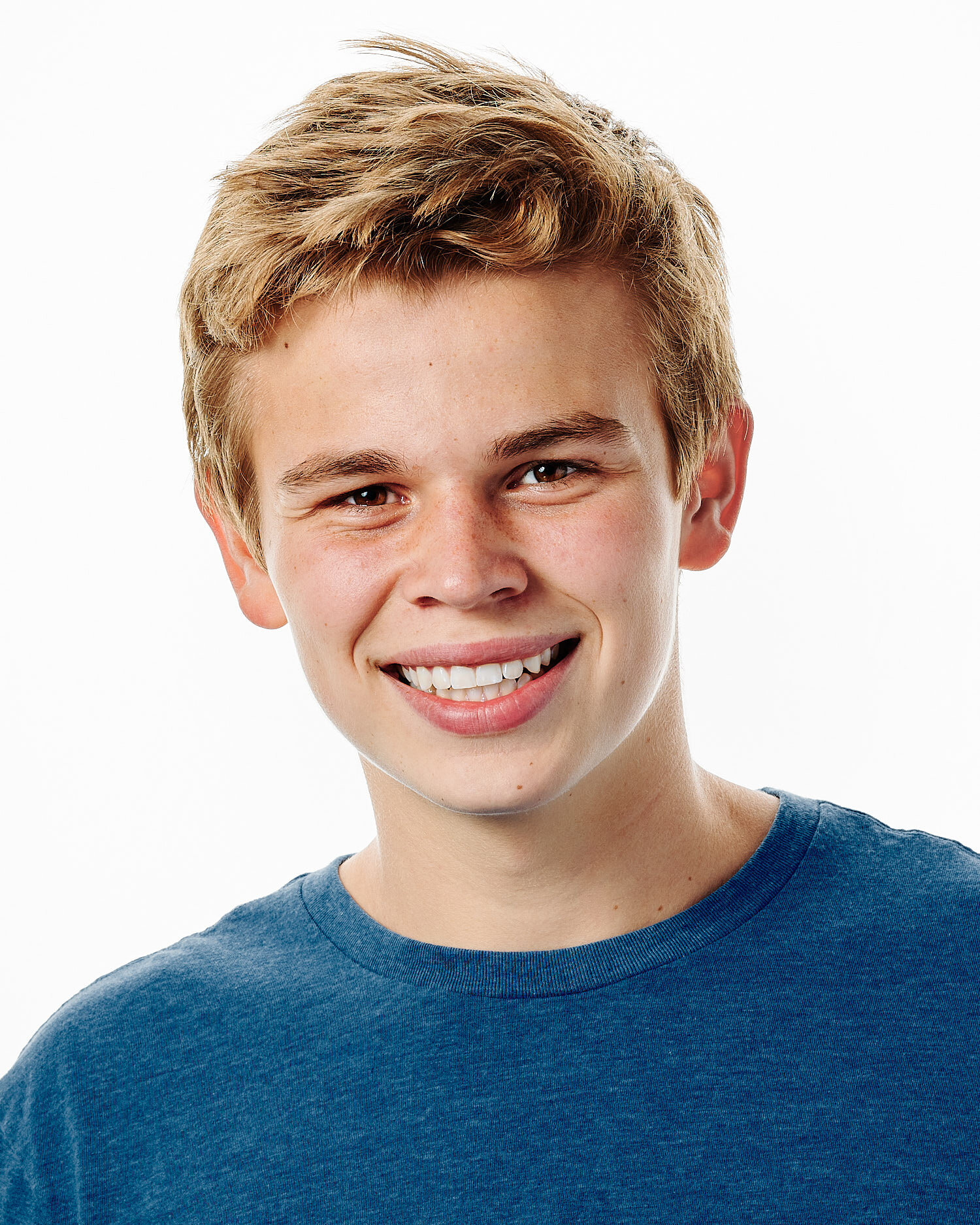  Max Peluso is posing for actor headshots against white background in a professional photography studio. He looks handsome and happy, he has blond hair and wears a blue t-shirt. 