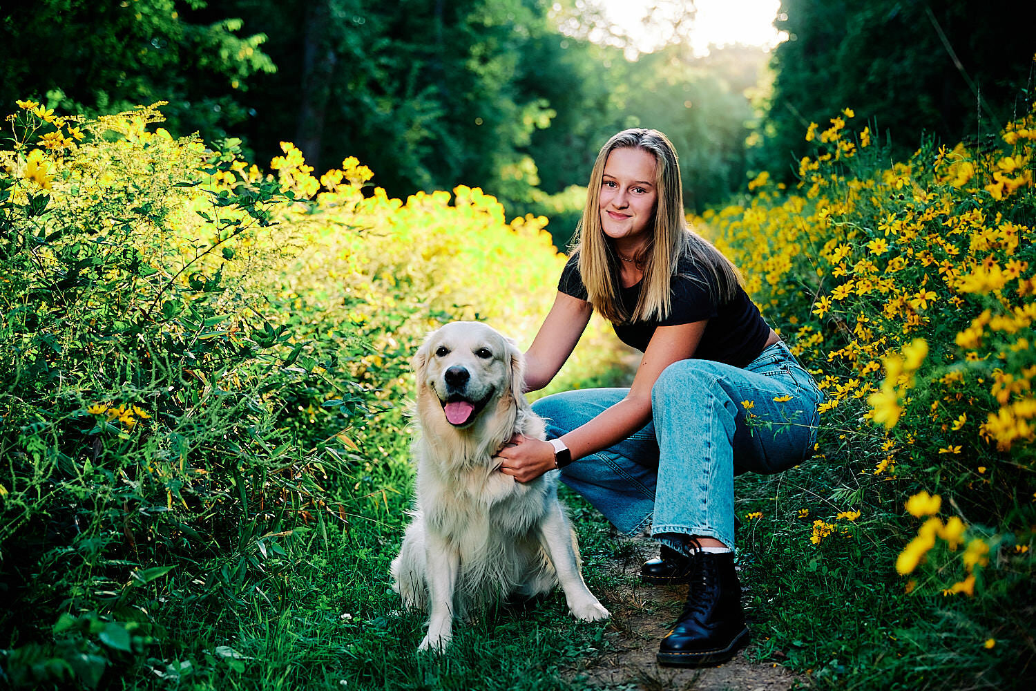  Alena Gurevich is posing for her high school senior pictures. It’s a beautiful sunset in the yellow flower field in the forest. She looks gorgeous, blonde hair, in her blue jeans and black t-shirt. 