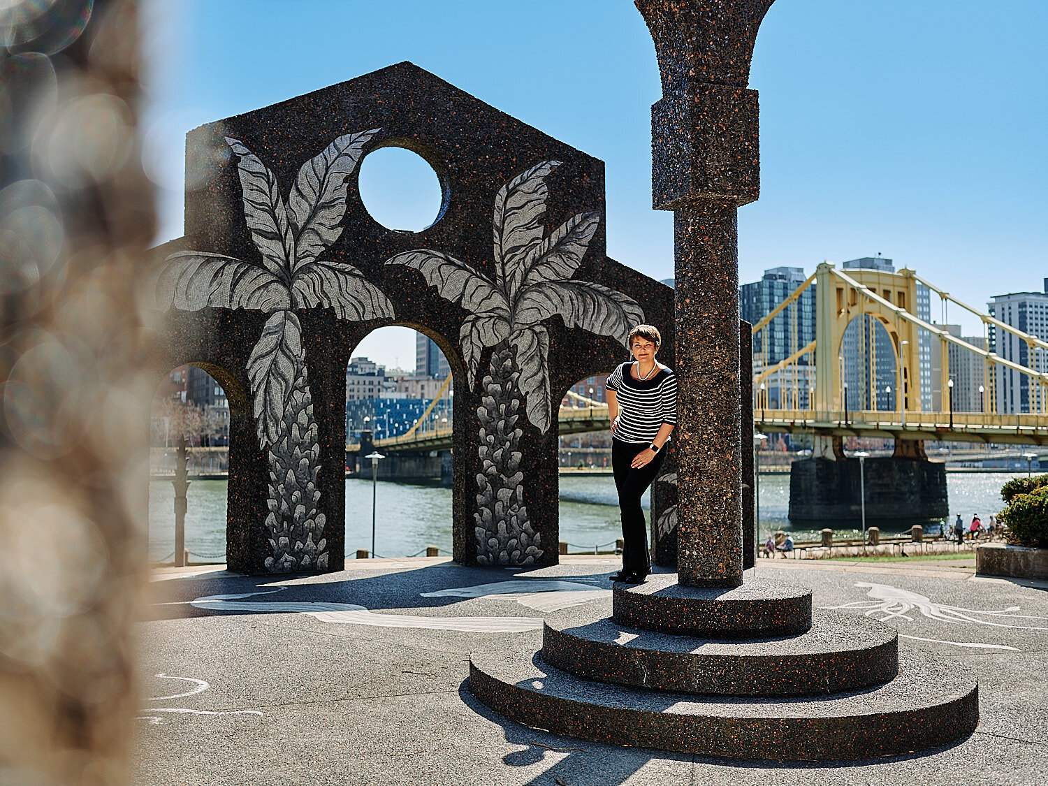  Pittsburgh downtown at midday in early April 2021 with yellow bridges in the background and cherry blossom in the foreground. A couple is photographing each other for happy environmental portraits. 