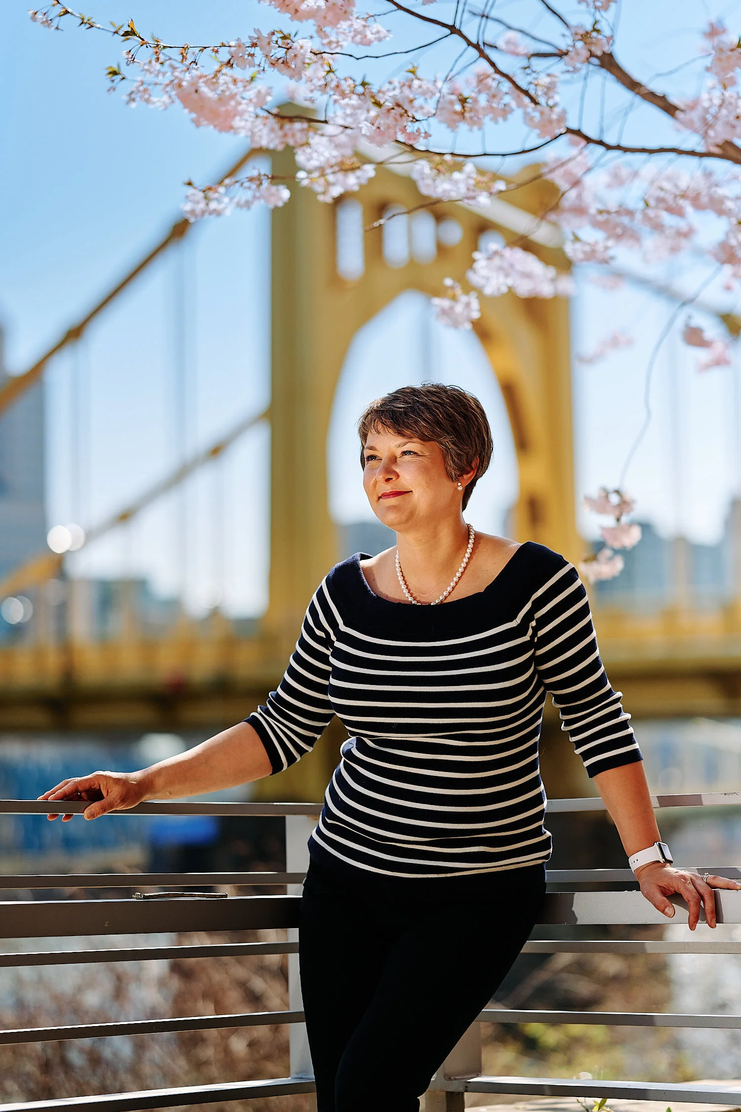  Pittsburgh downtown at midday in early April 2021 with yellow bridges in the background and cherry blossom in the foreground. A couple is photographing each other for happy environmental portraits. 